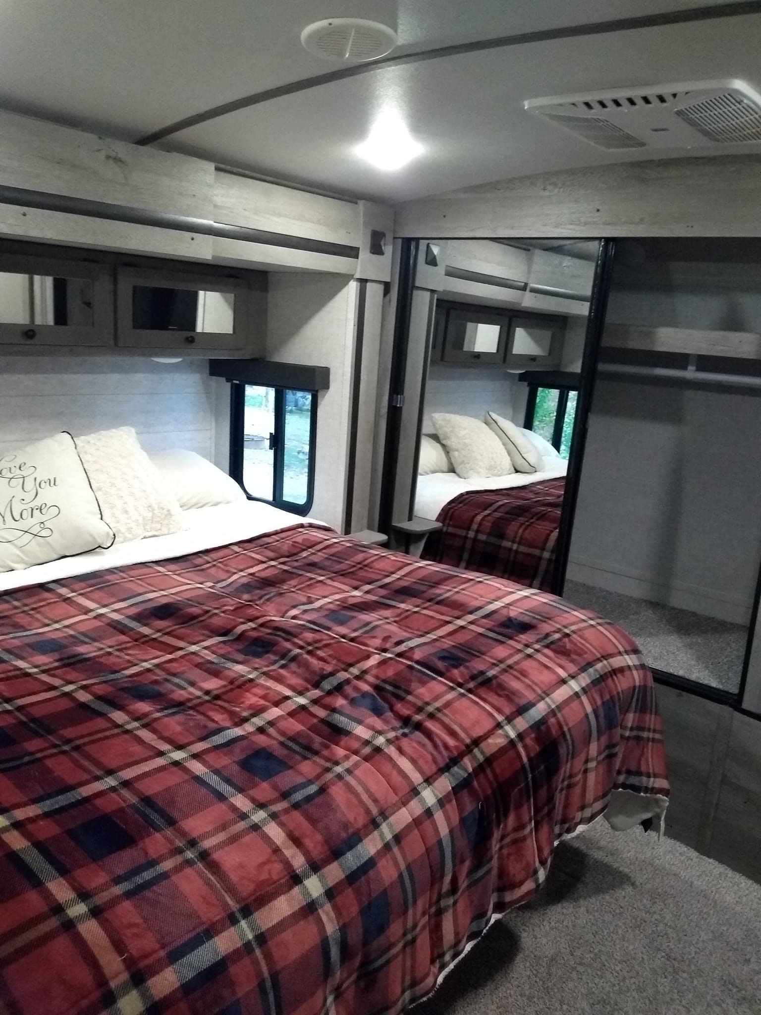 Step into comfort! This RV rental features a cozy bedroom with plaid bedding, mirrored storage, and compact design.. Keystone Outback 2020