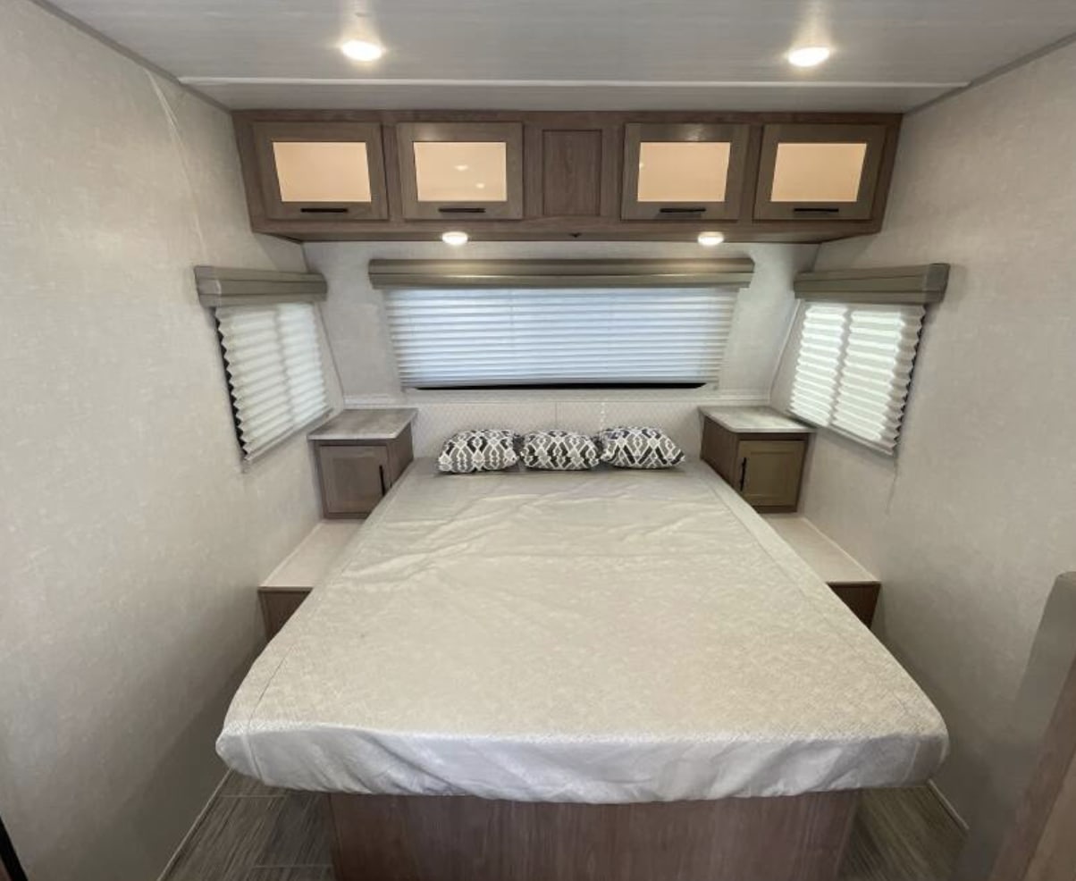 Cozy RV rental bedroom with a comfortable bed, overhead cabinets, and windows with blinds on each side.. Forest River No Boundaries 19.5 2022