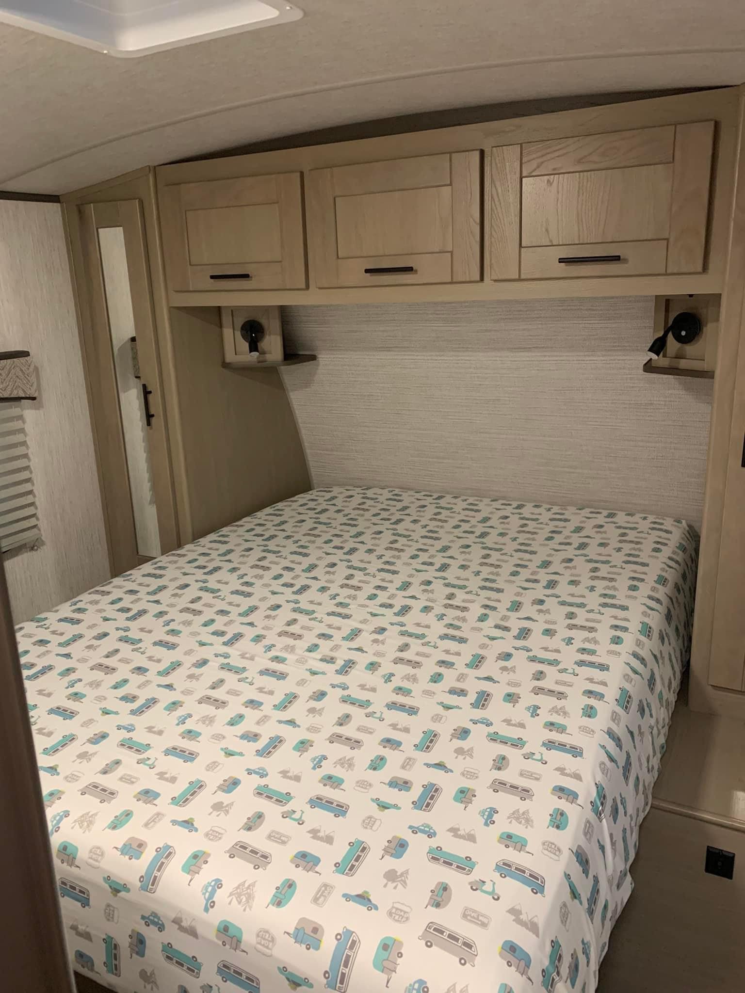 RV rental bedroom with camper-themed sheets, overhead storage, and reading lights, ideal for travel.. Heartland RVs Sundance Ultra Lite 2021