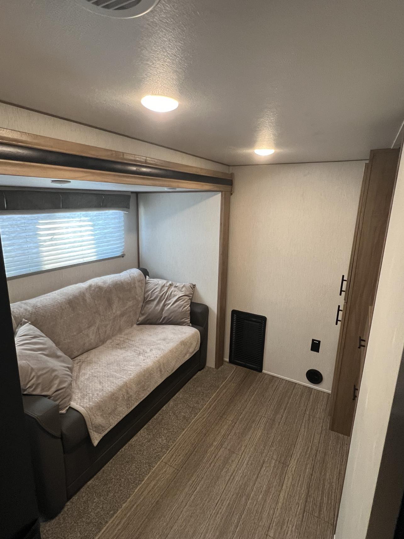 This RV rental bunk area/living space features a cozy couch, window with blinds, and mixed flooring. Ideal for comfort.. Forest River Sabre 2023