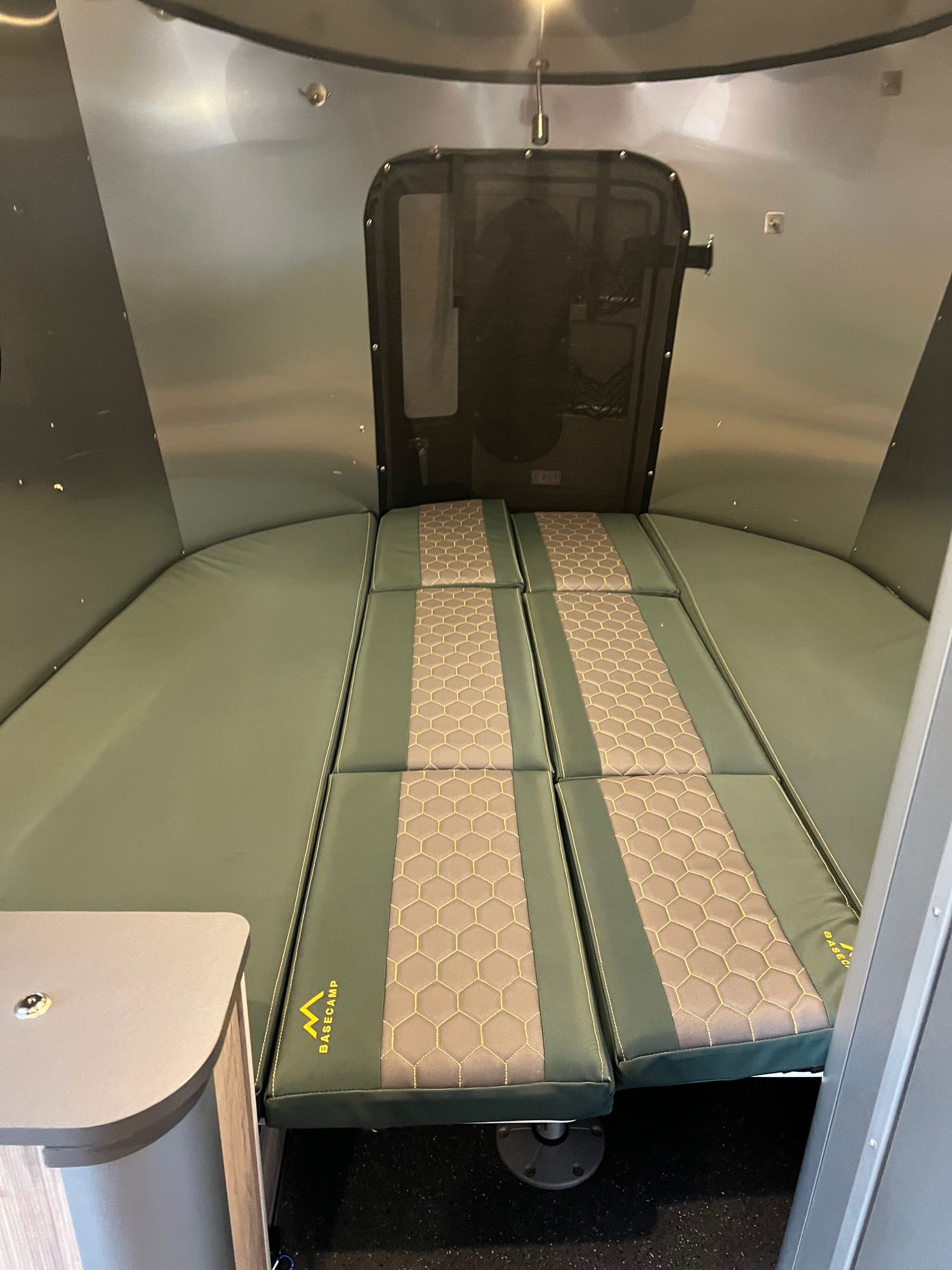 Airstream Basecamp RV rental interior with modular green and patterned cushions forming a bed, set against metallic walls.. Airstream Basecamp 2020