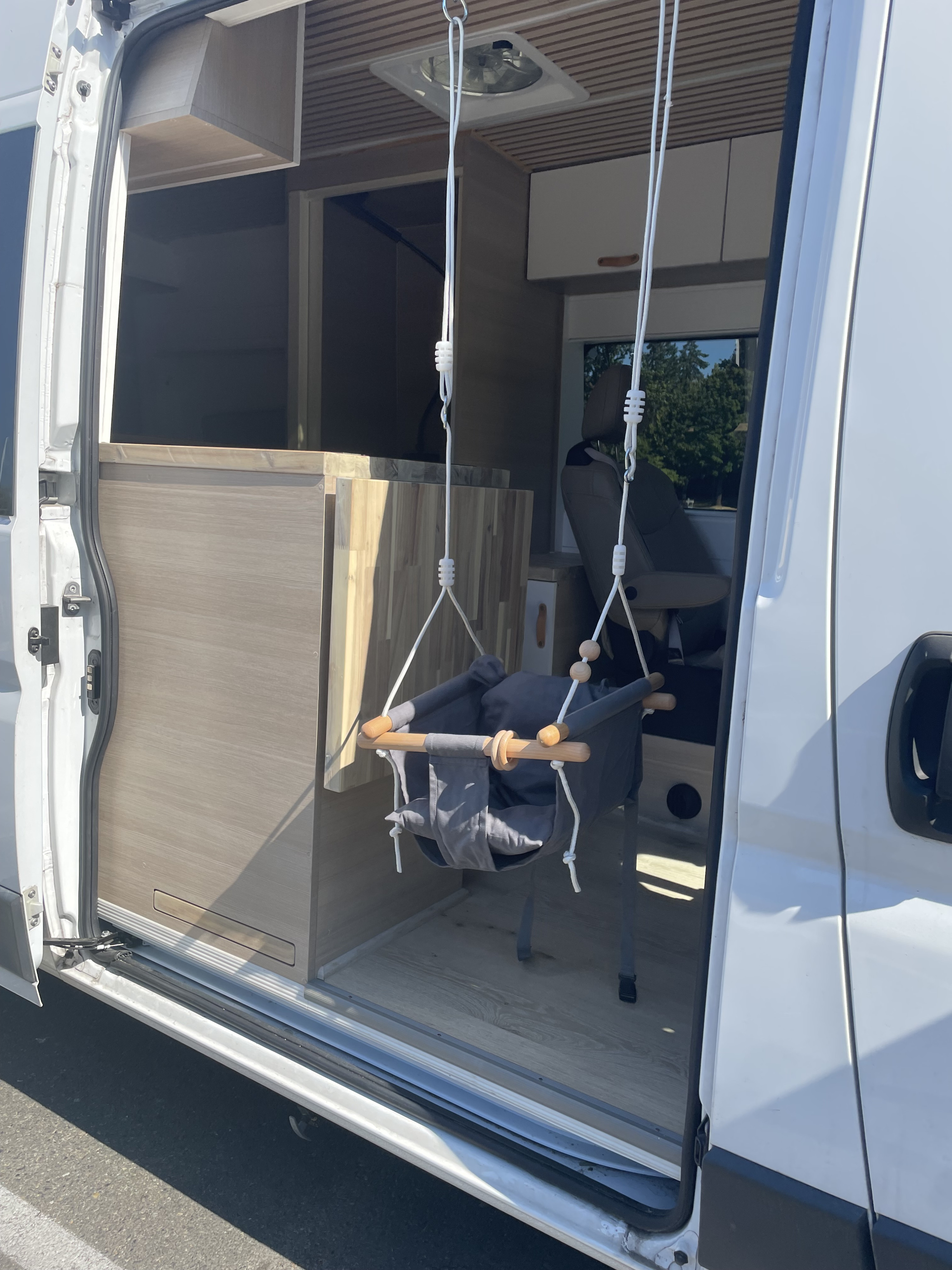 RV rental: Inside a camper van, a baby swing hangs from the ceiling vent. Perfect for family van life & travel adventures.. Vanberry Promaster 2018