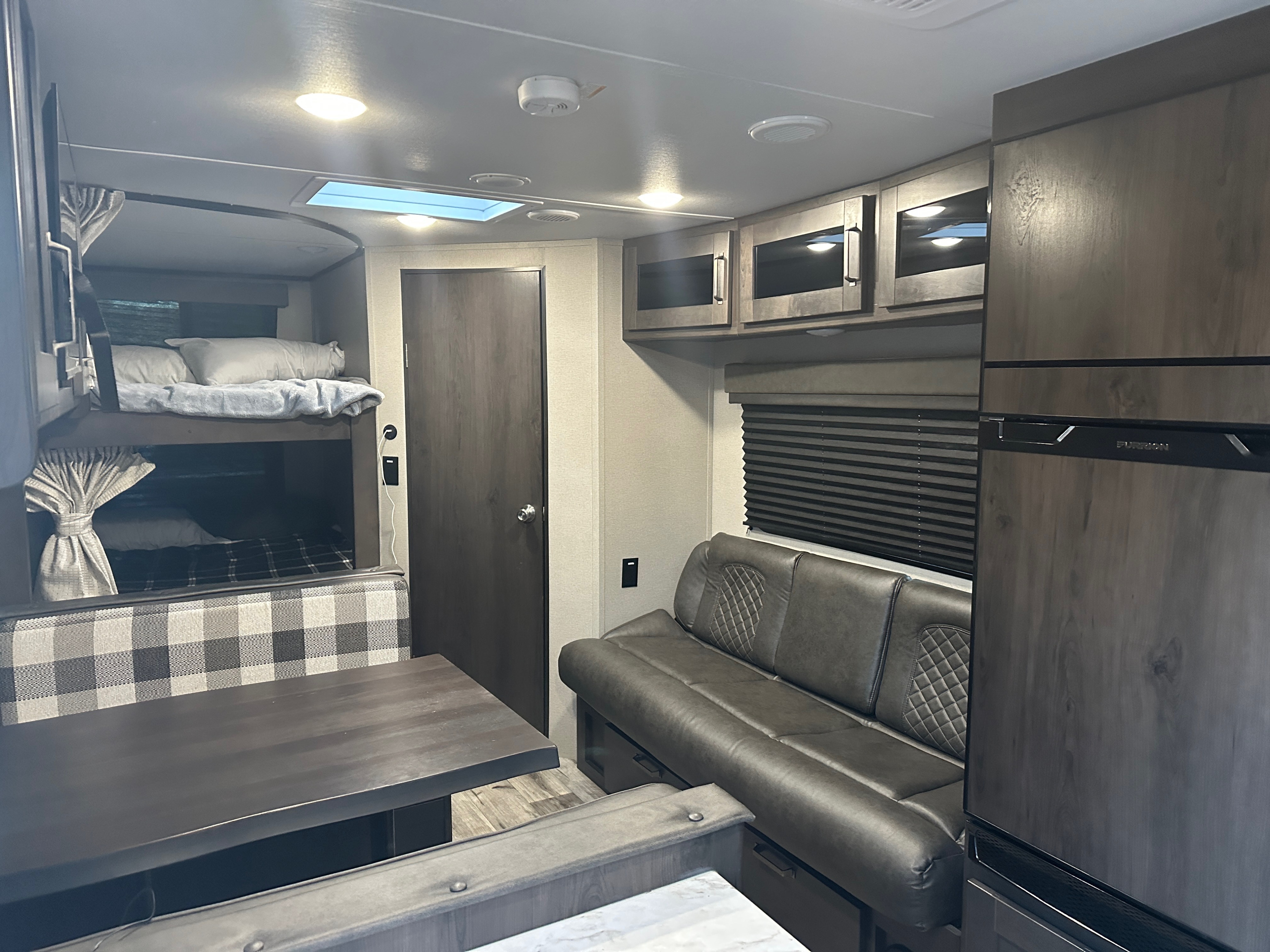 Inside this modern rv rental: bunk beds, a plaid dinette, plush sofa, and fridge. Perfect for road trips and family fun.. Grand Design Transcend Xplor 2023