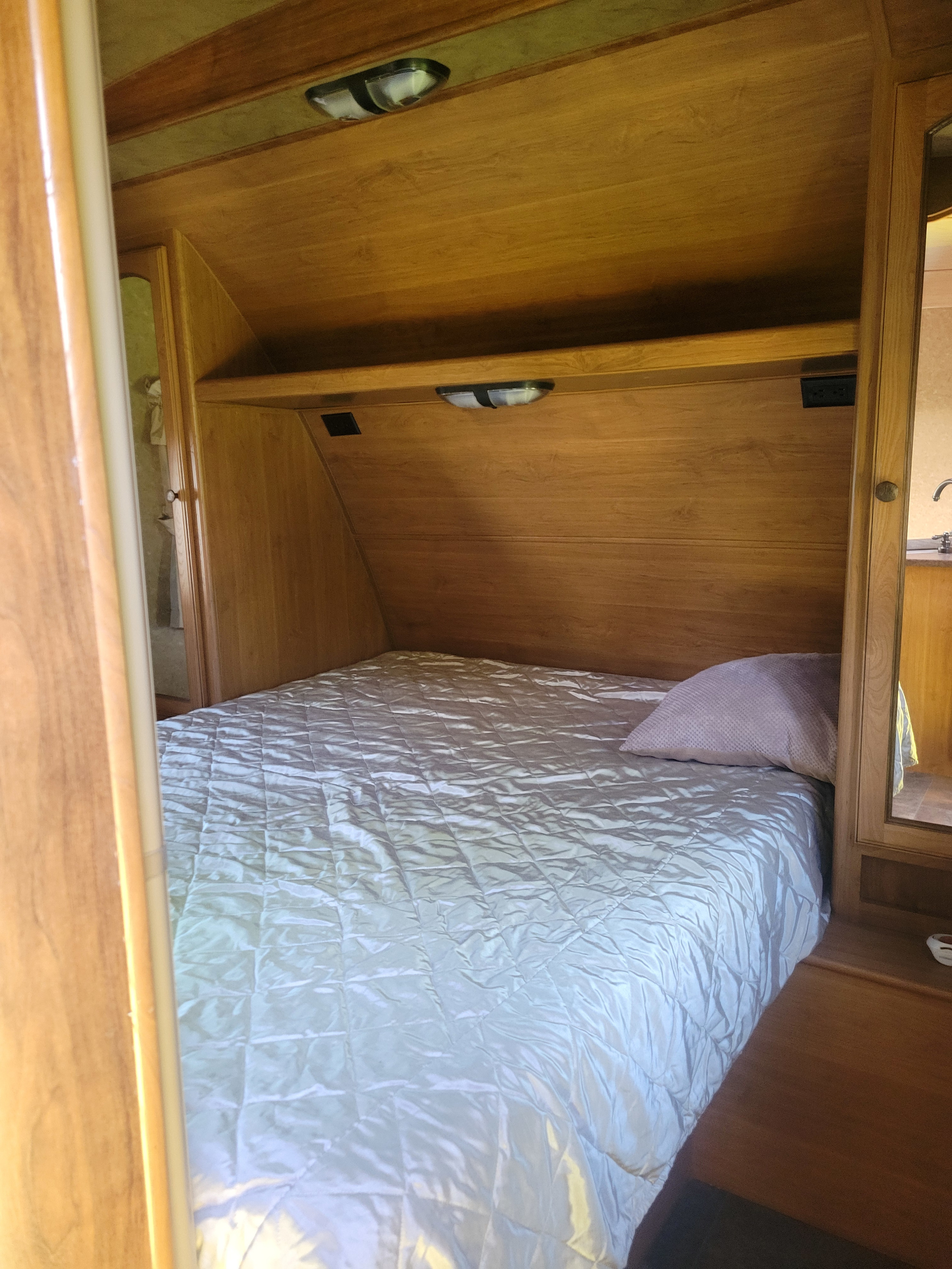 This compact RV rental bedroom features a cozy bed, wood paneling, an overhead shelf, and built-in lighting.. Crossroads RV Sunset Trail Super Lite 2015
