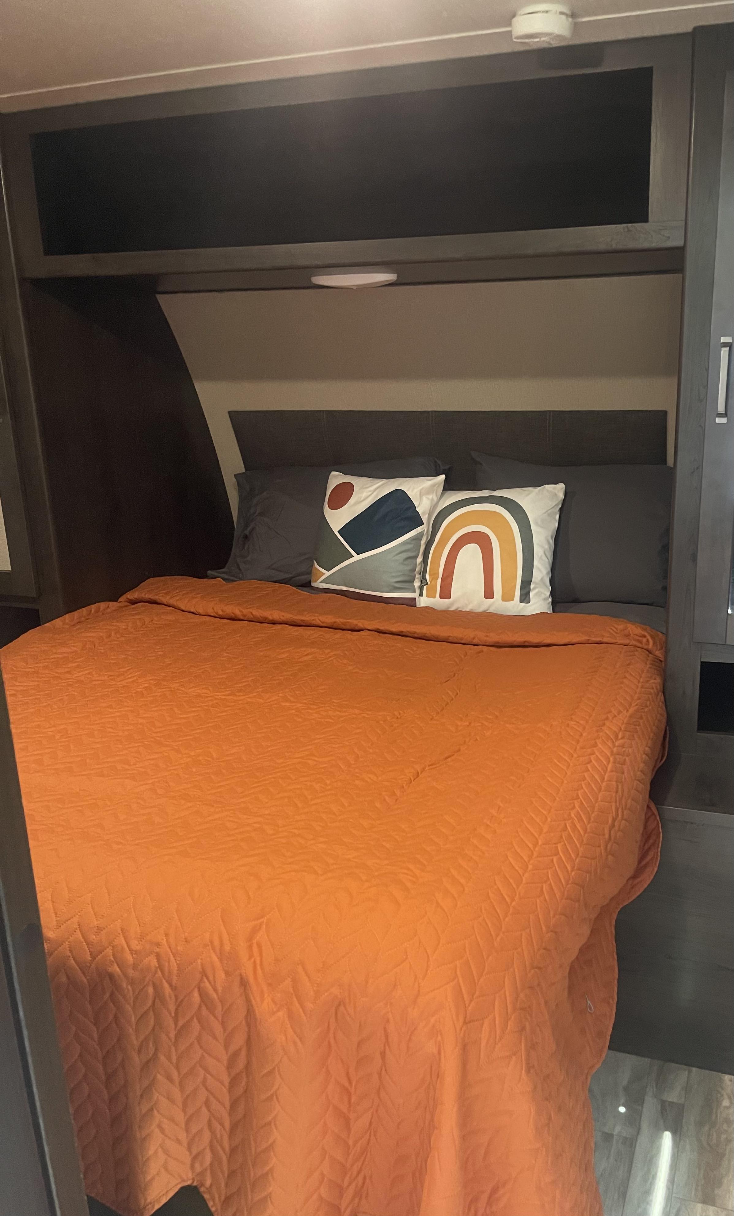 Inside an RV rental: a neat bedroom with an orange bedspread and modern accent pillows.. Grand Design Transcend Xplor 2023