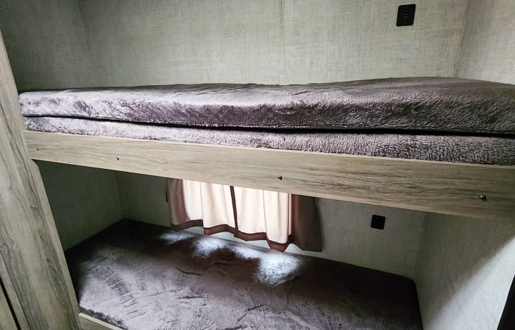 Inside this RV rental, comfortable bunk beds feature soft, plush bedding, a window with curtains, and convenient wall outlets.. Gulf Stream Kingsport 2022