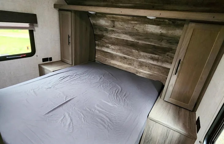 Cozy RV rental bedroom with a large bed, rustic wood headboard, side cabinets, and window. Ideal for road trips.. Gulf Stream Kingsport 2022