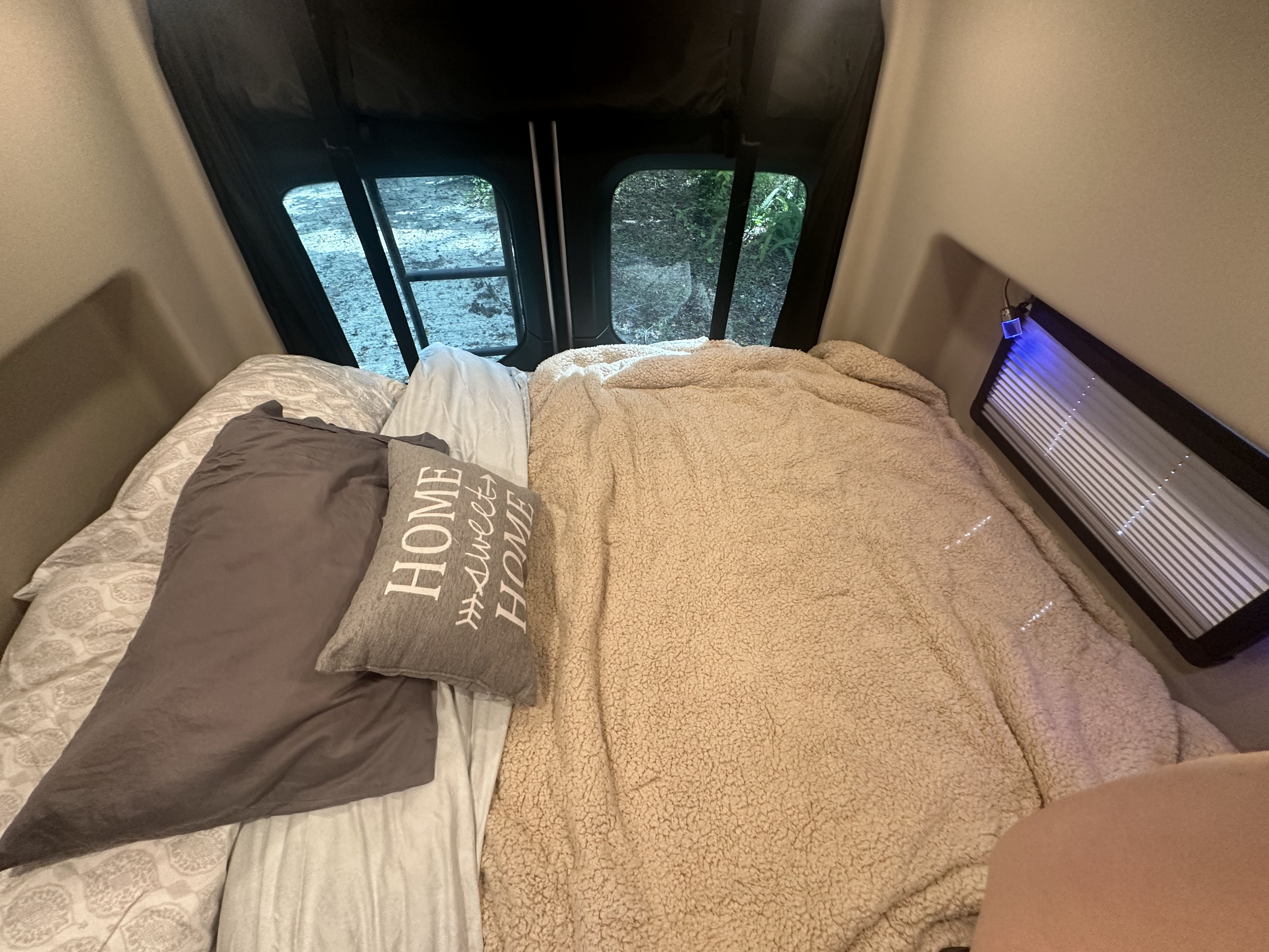 Cozy rv rental bed with "HOME sweet HOME" pillow, fluffy blanket, and nature views through the windows.. Mercedes-Benz Jayco Terrain 2023