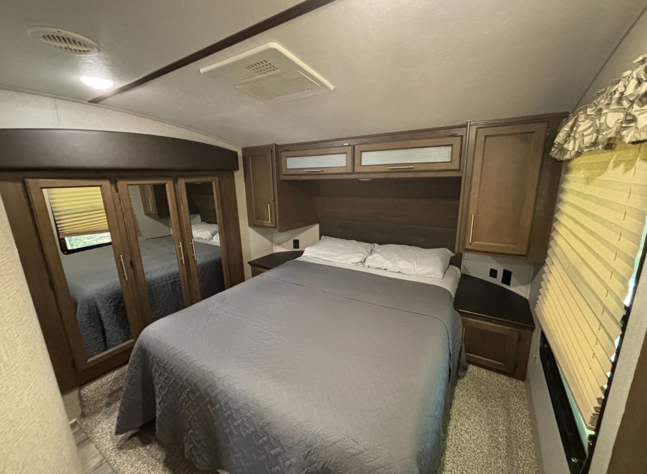 Cozy RV rental bedroom with a comfortable bed, mirrored closet, overhead cabinets, and window blinds.. Keystone RV Cougar 2019