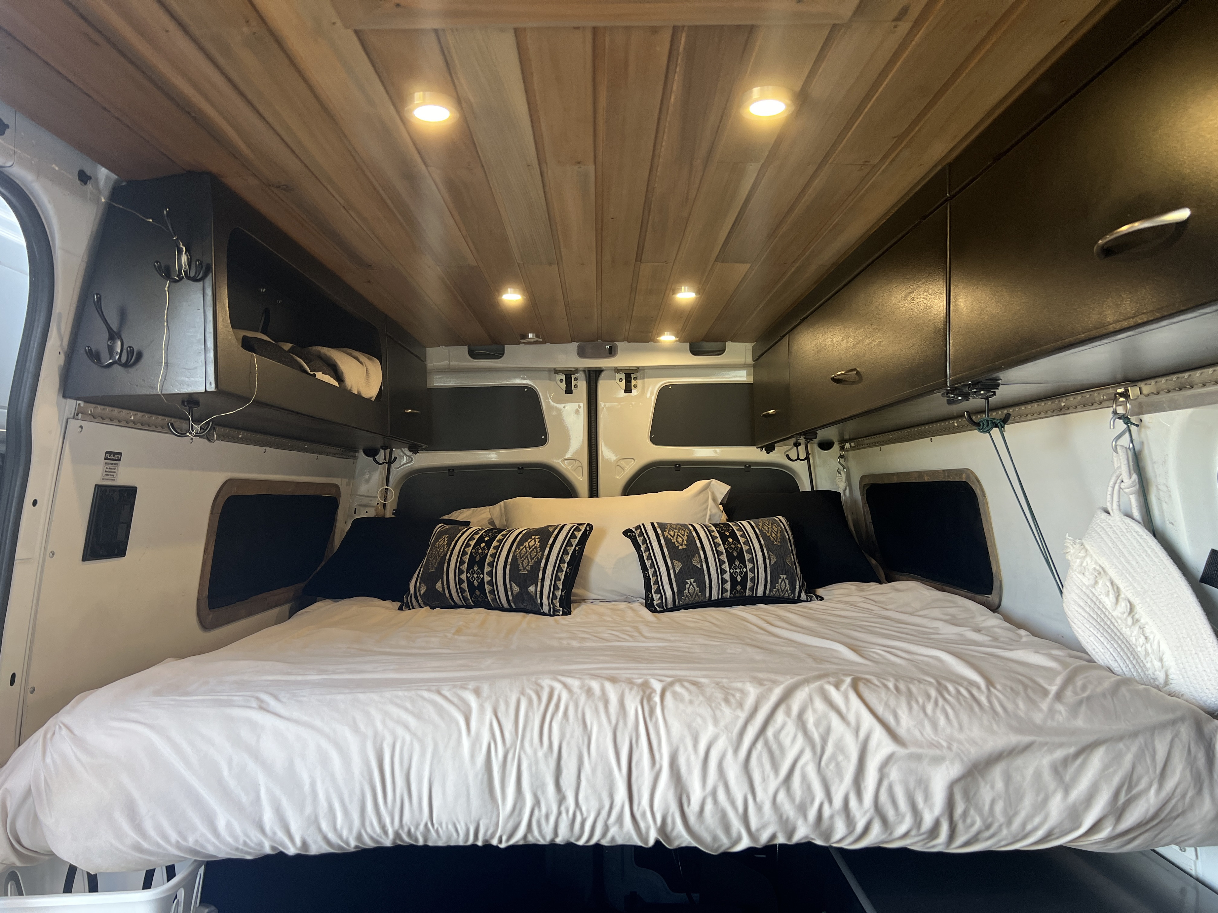 Cozy RV rental interior: bedroom with wooden ceiling, recessed lights, and overhead storage. Ideal for travel.. Freightliner Sprinter 2016