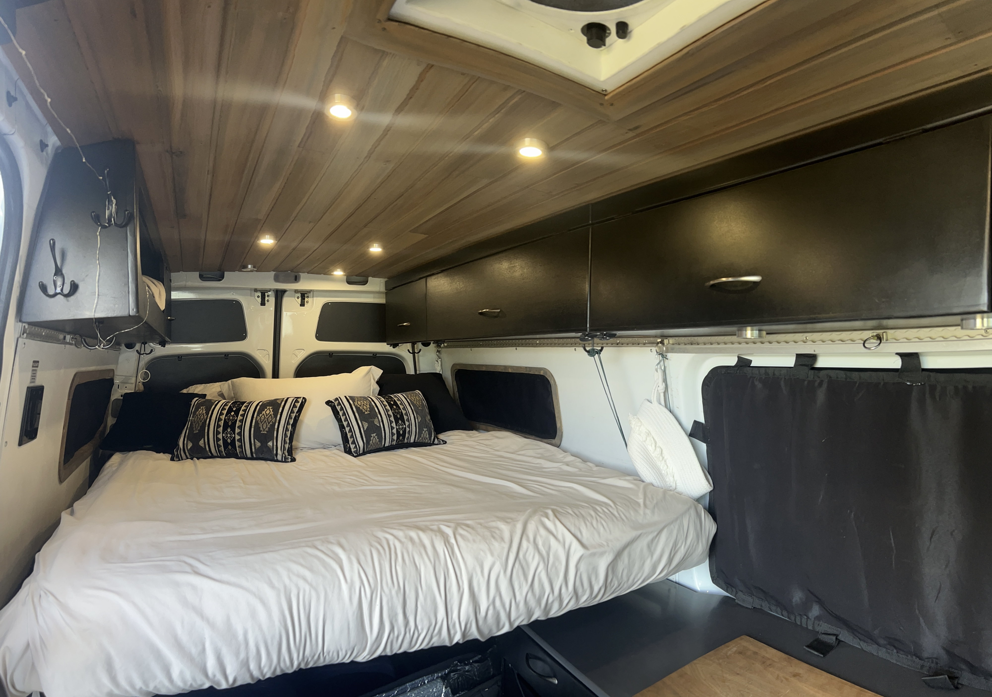 Cozy RV rental interior with a comfortable bed, wooden ceiling lights, and overhead storage, perfect for mobile travel.. Freightliner Sprinter 2016