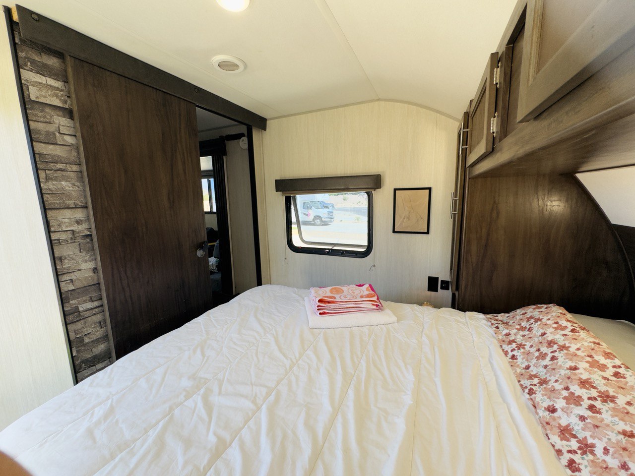 View of a comfortable RV rental bedroom interior, featuring a bed, barn-style door, and side window.. Forest River Cherokee Grey Wolf 2021