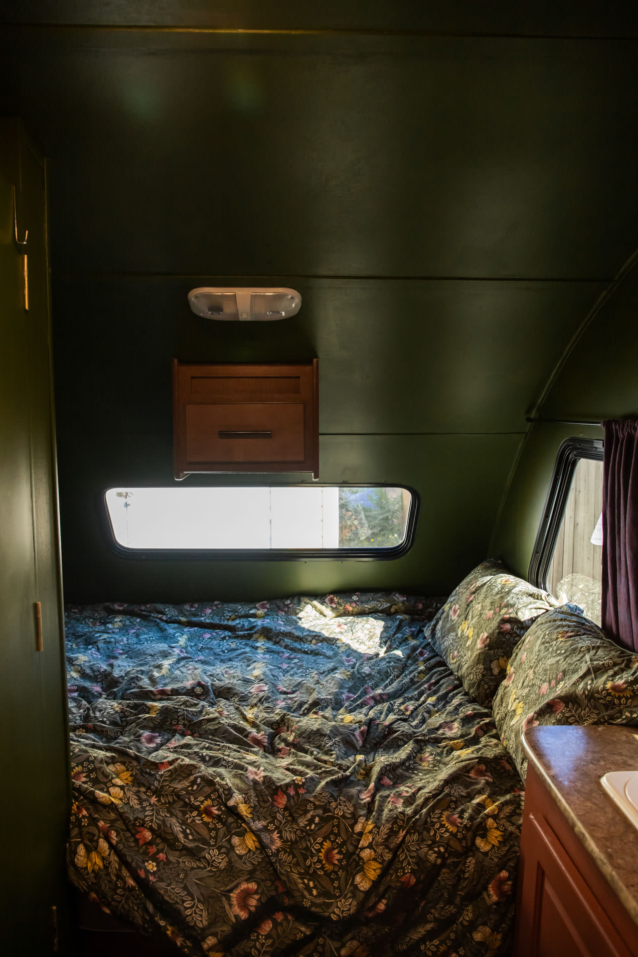 Inside an RV rental: a cozy bedroom with dark green walls, floral bedding, and sunlit windows, ready for a comfortable stay.. Forest River R-pod 2013