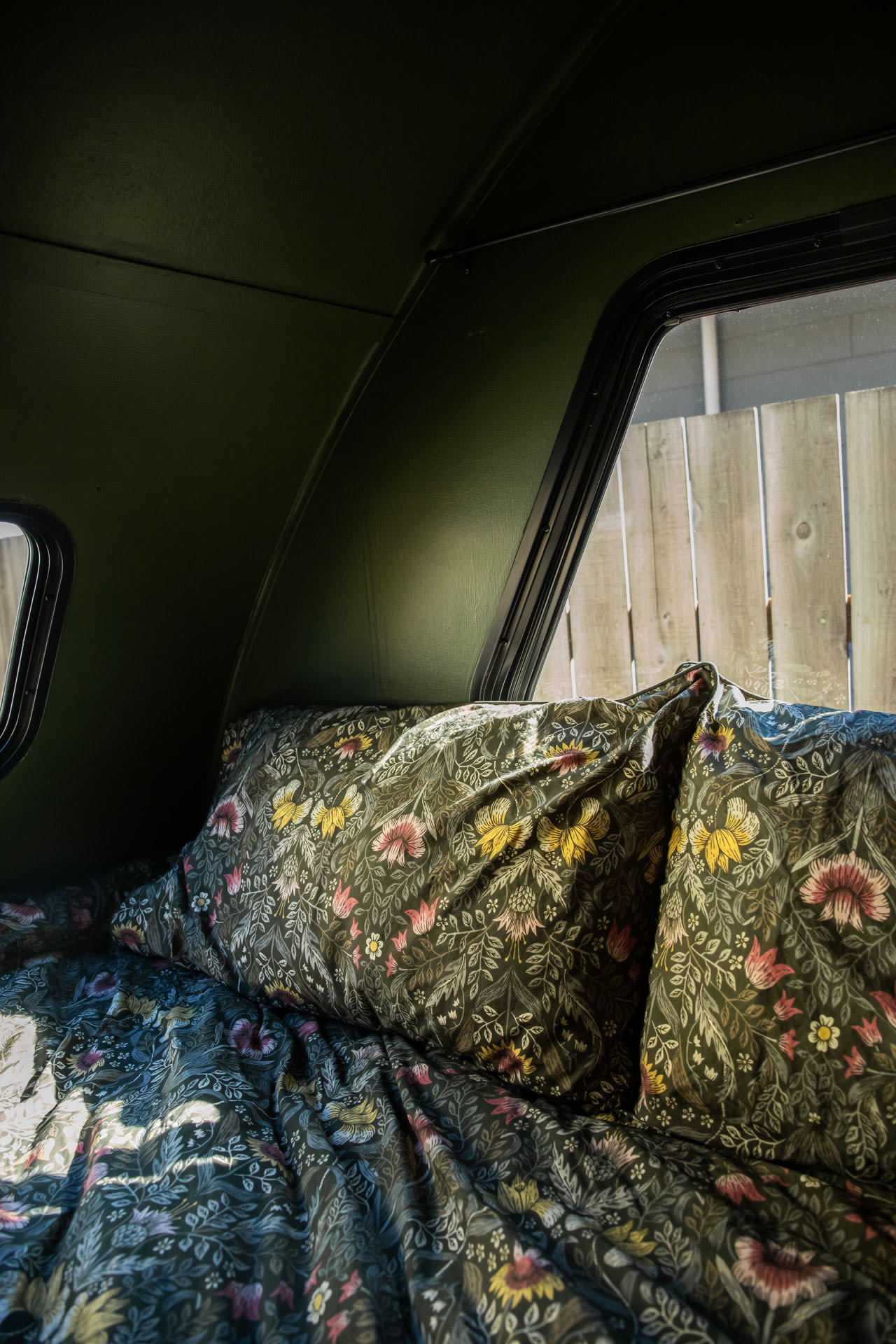 This RV rental offers a cozy sleeping area with dark green walls, a window, and vibrant floral bed linens.. Forest River R-pod 2013