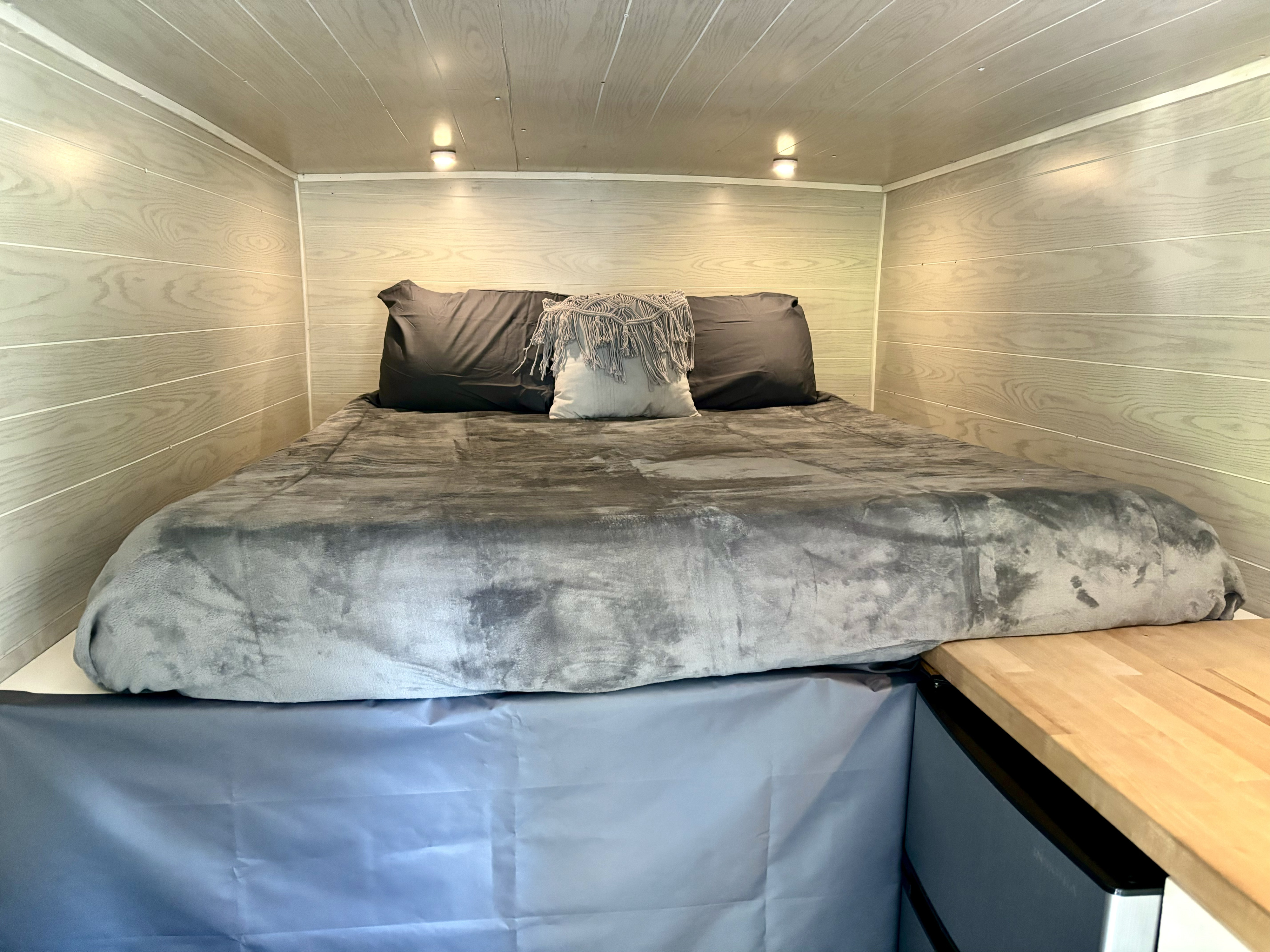 Cozy RV rental bedroom featuring a grey bed, wood-paneled walls/ceiling, and convenient under-bed storage.. Ford E350 Box Van 2008