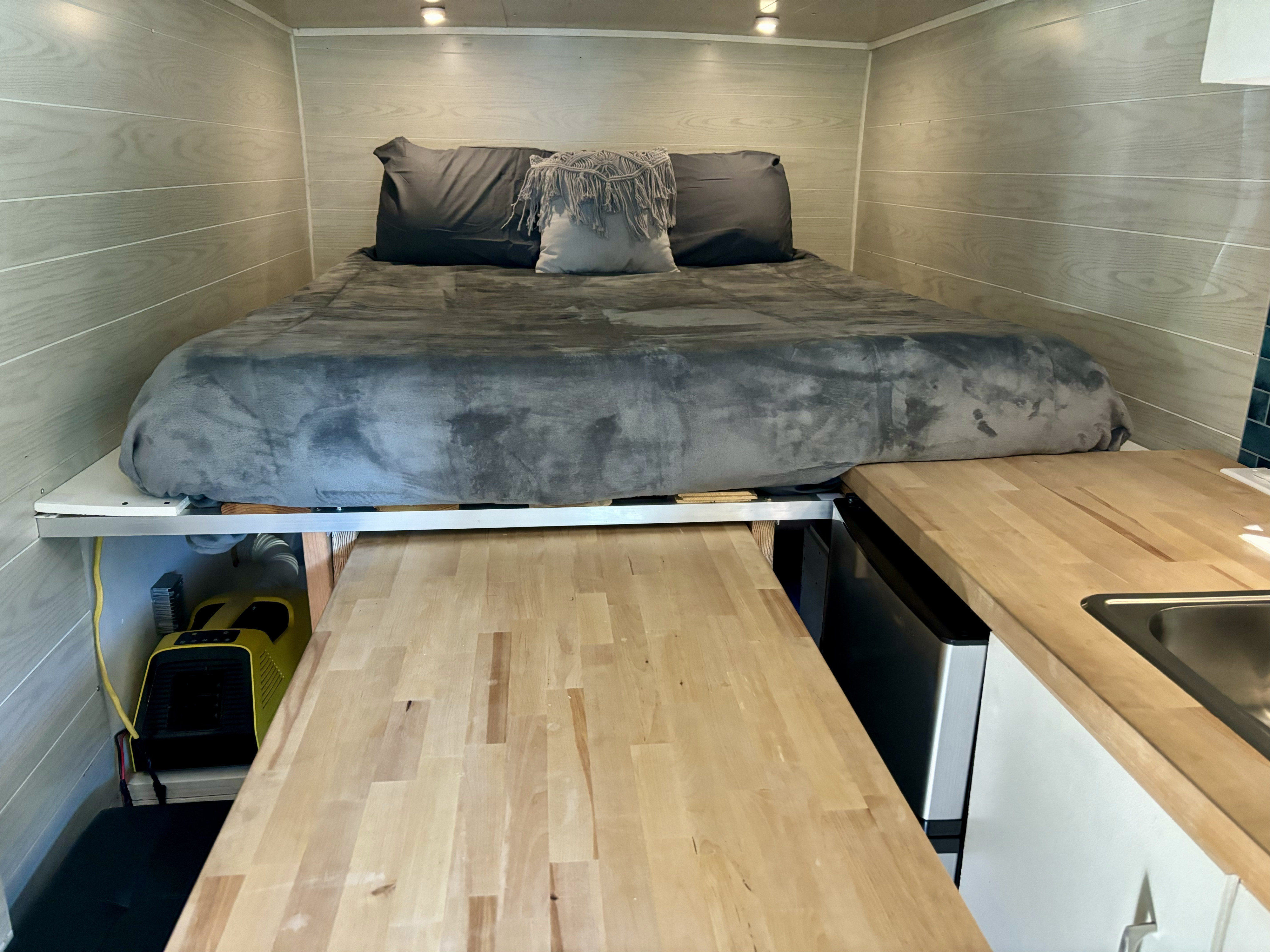 RV rental: Interior with elevated bed, light wood walls, lower wooden table, kitchen, sink, mini-fridge, and yellow heater.. Ford E350 Box Van 2008