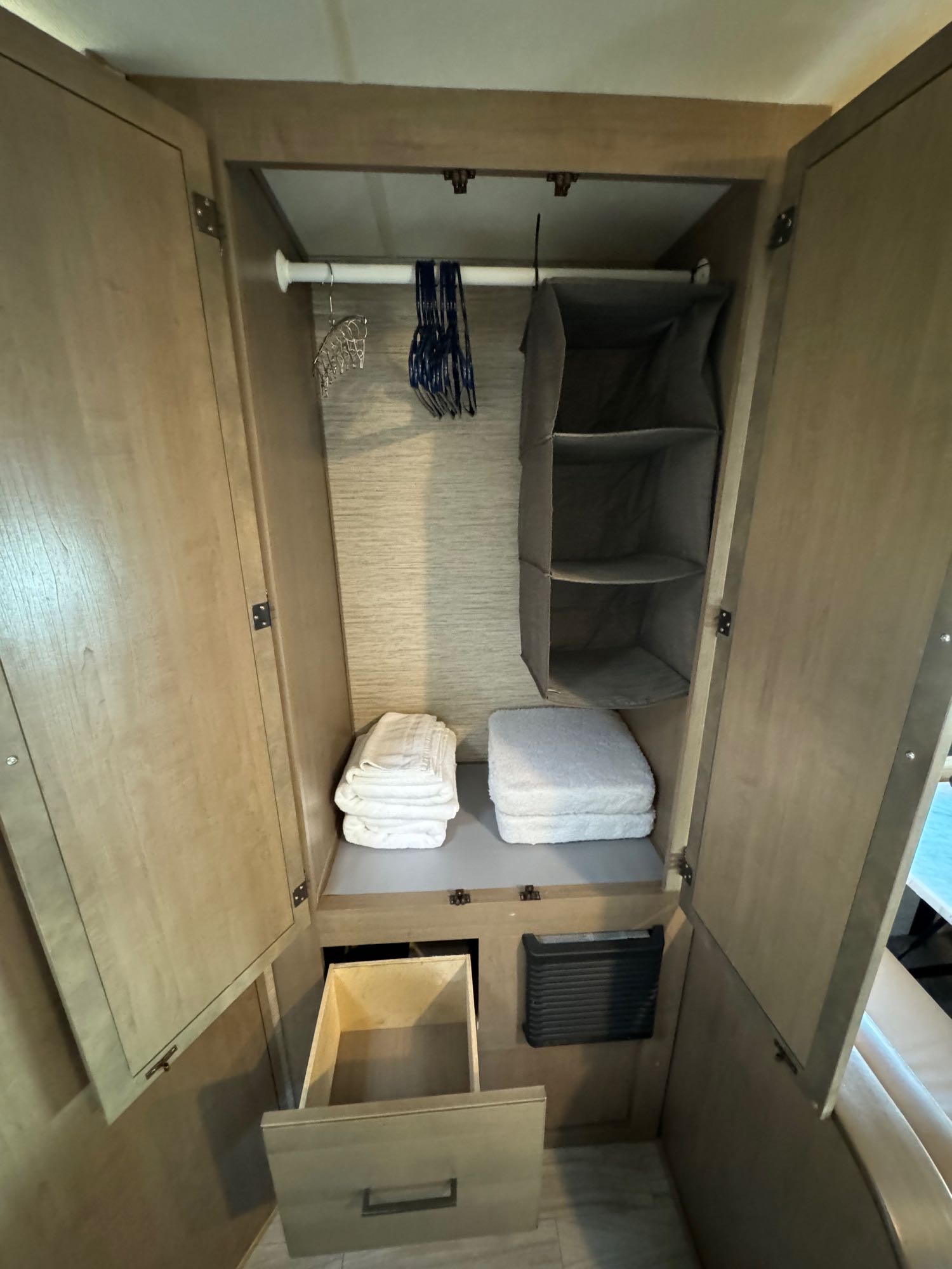 This RV rental closet offers organized storage: a hanging rod with hangers, a fabric organizer, folded towels, and a drawer.. Thor Motor Coach Coleman 2021