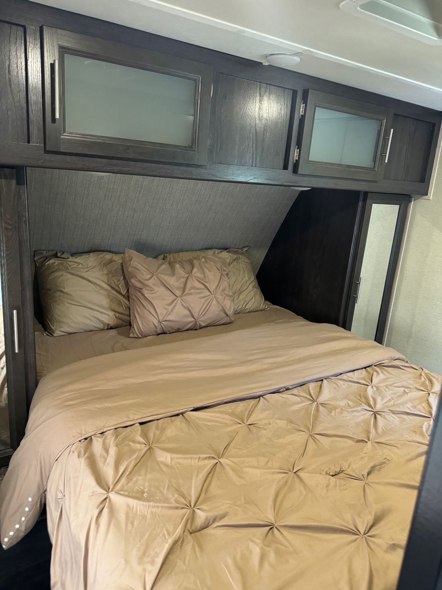 Cozy RV rental bedroom featuring warm tan bedding, overhead cabinets with frosted glass, and built-in side storage.. Dutchmen Kodiak Ultralight 2018
