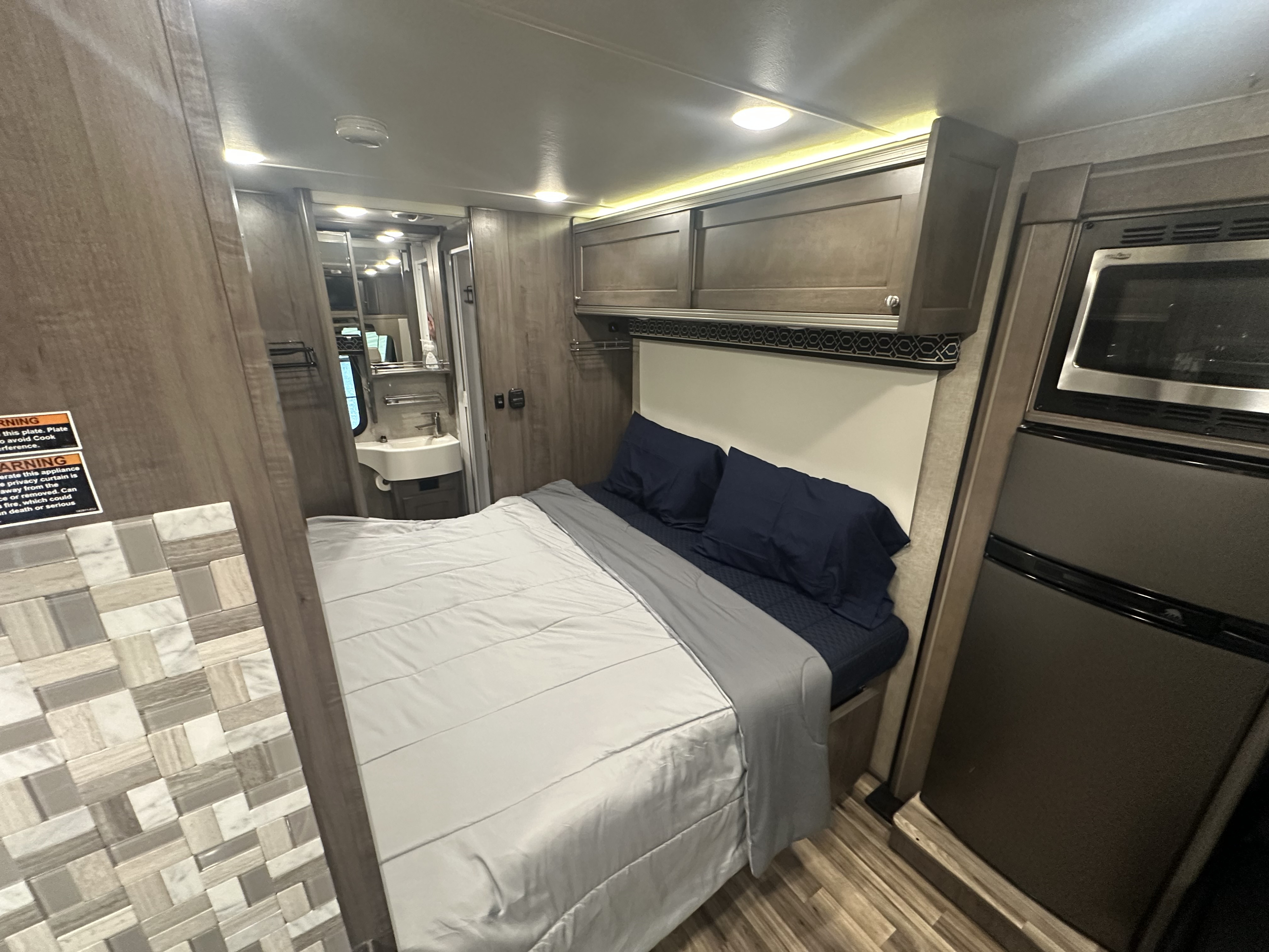 Compact rv rental interior with a comfy bed, overhead storage, kitchen appliances, and a small bathroom.. Winnebago Fuse 2017