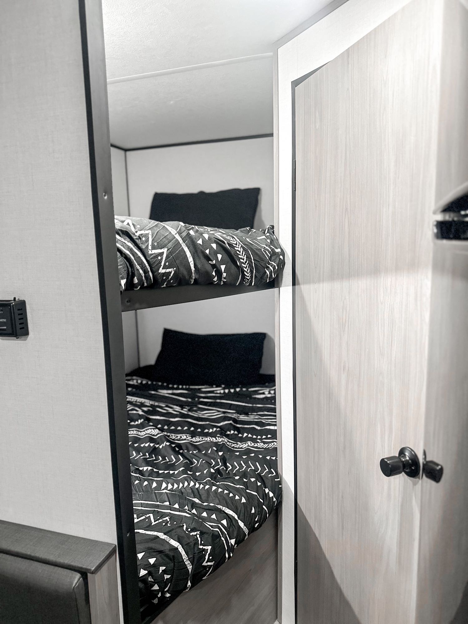 Spacious RV rental bunk beds, neatly made with black & white bedding, ideal for family trips. Control panel visible.. Dutchmen Coleman Lantern LT 2024