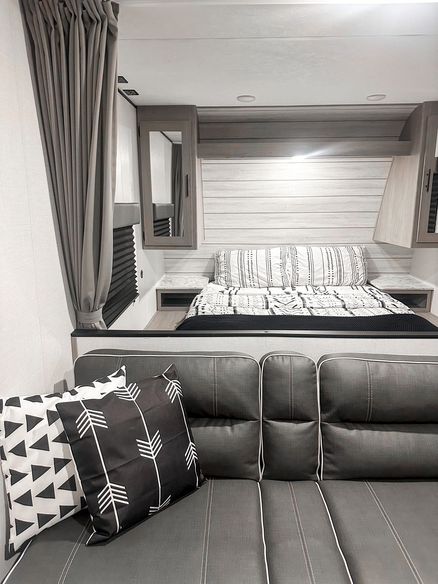 Modern RV rental interior featuring a bed with patterned bedding, sleek wood-paneled walls, and a comfortable gray sofa.. Dutchmen Coleman Lantern LT 2024