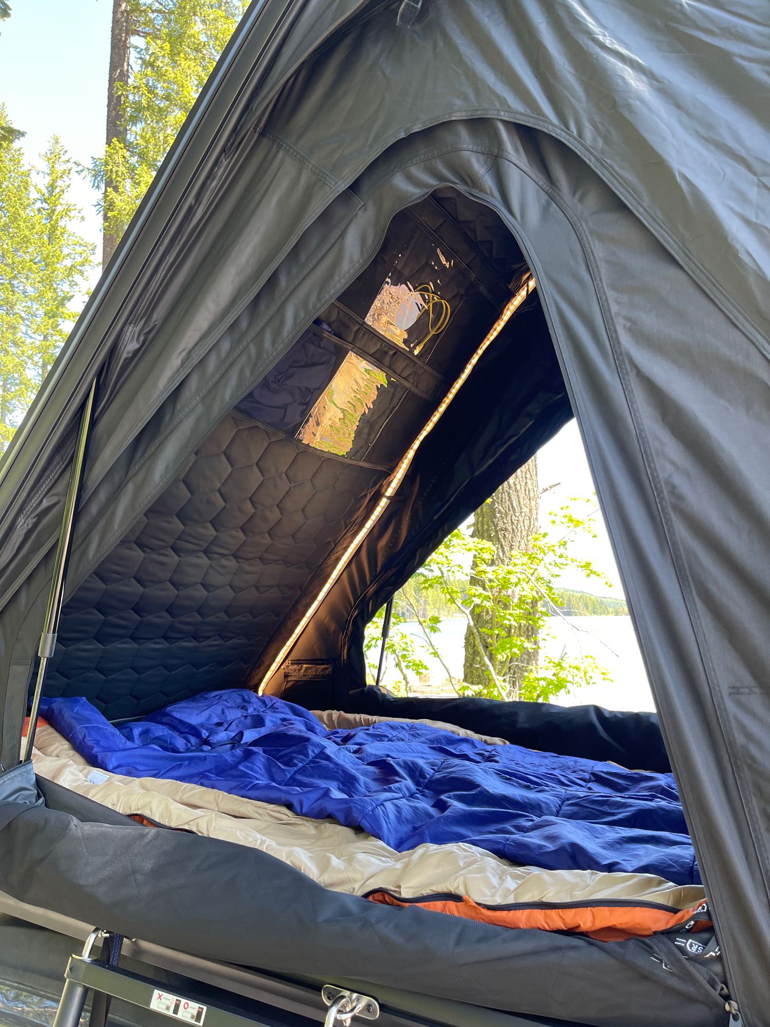 RV rental adventure: A cozy rooftop tent setup with bed, quilted ceiling, and a scenic lake view.. Subaru Outback 2014