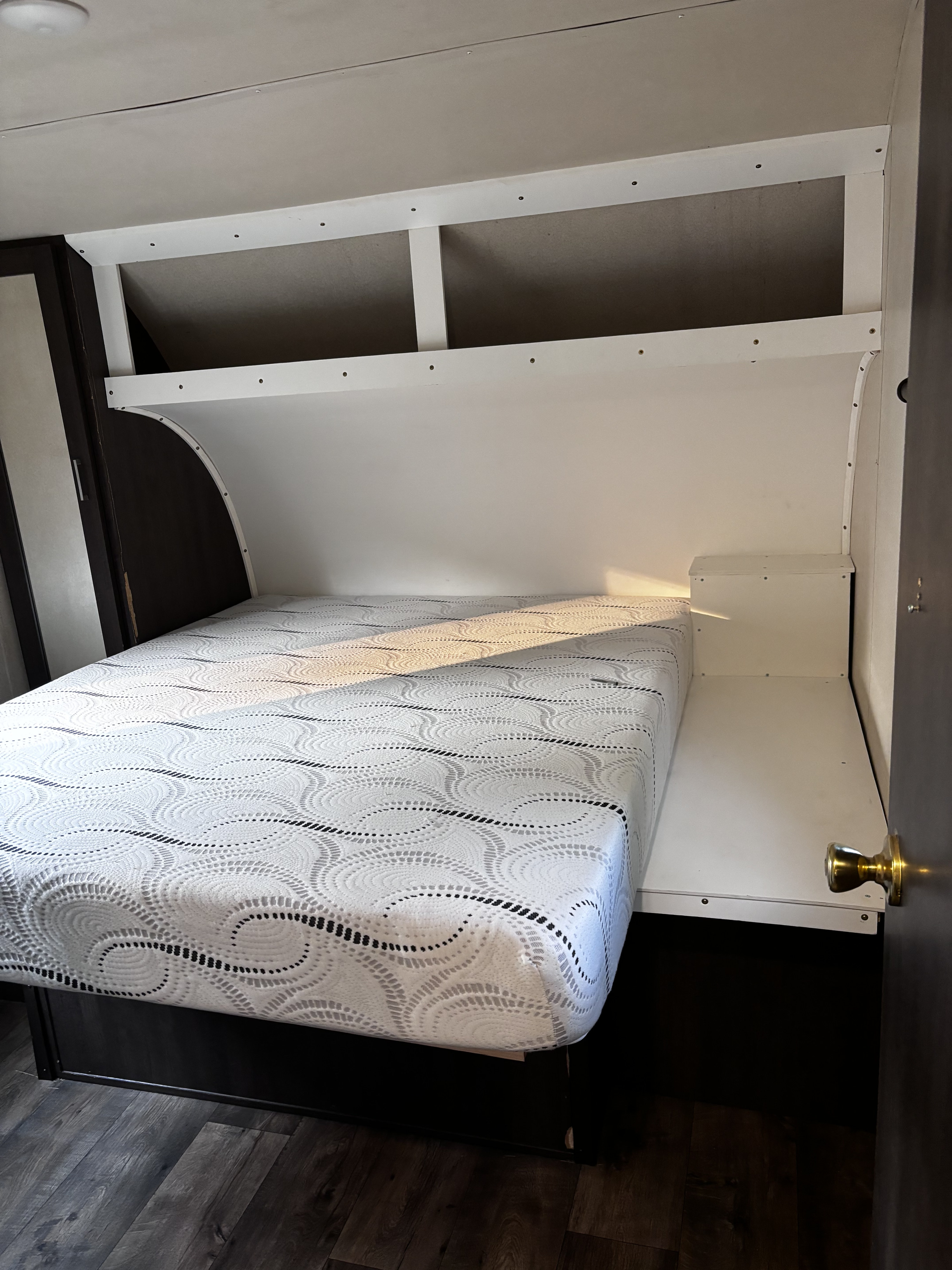 RV rental bedroom: comfortable bed, built-in overhead shelving, and a compact bedside table, optimizing space.. Forest River Wildwood 2017