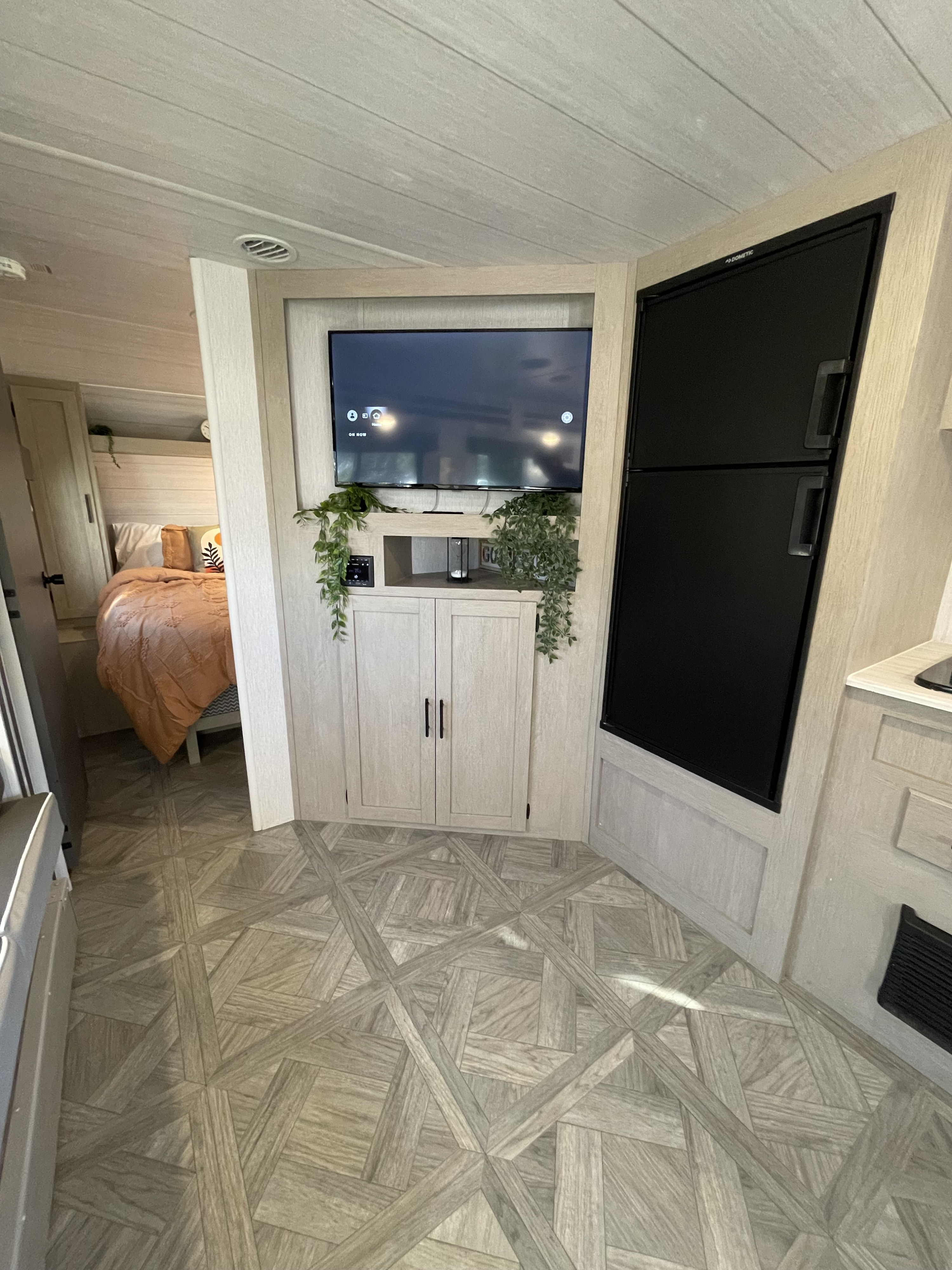 RV rental: Modern interior with a light wood plank ceiling, geometric floor, TV, fridge, and bedroom access.. Forest River Wildwood X-Lite 2024