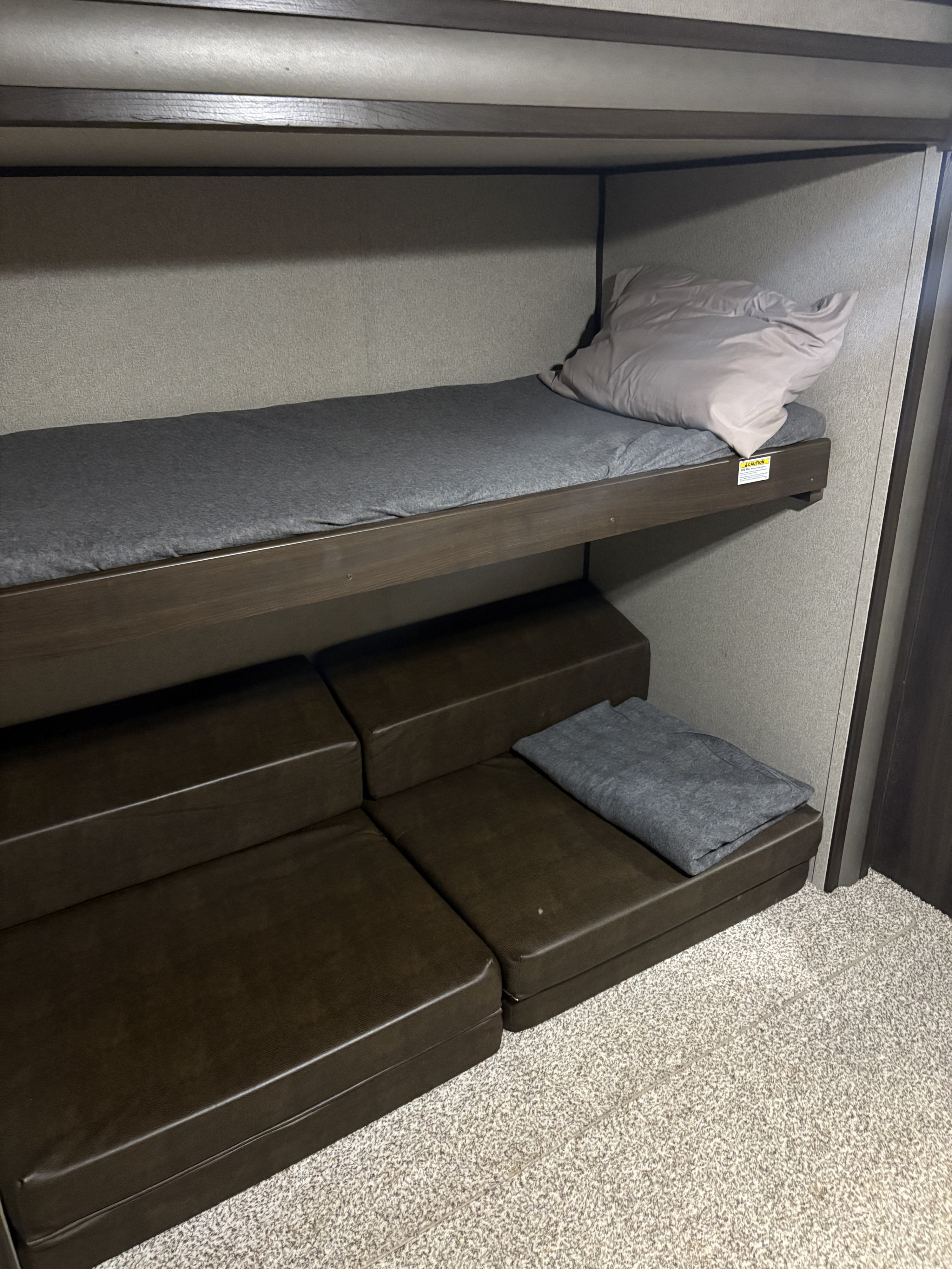 Comfortable RV rental bunk bed with grey mattress, plus versatile brown seating/sleeping cushions below.. Keystone RV Summerland 2018