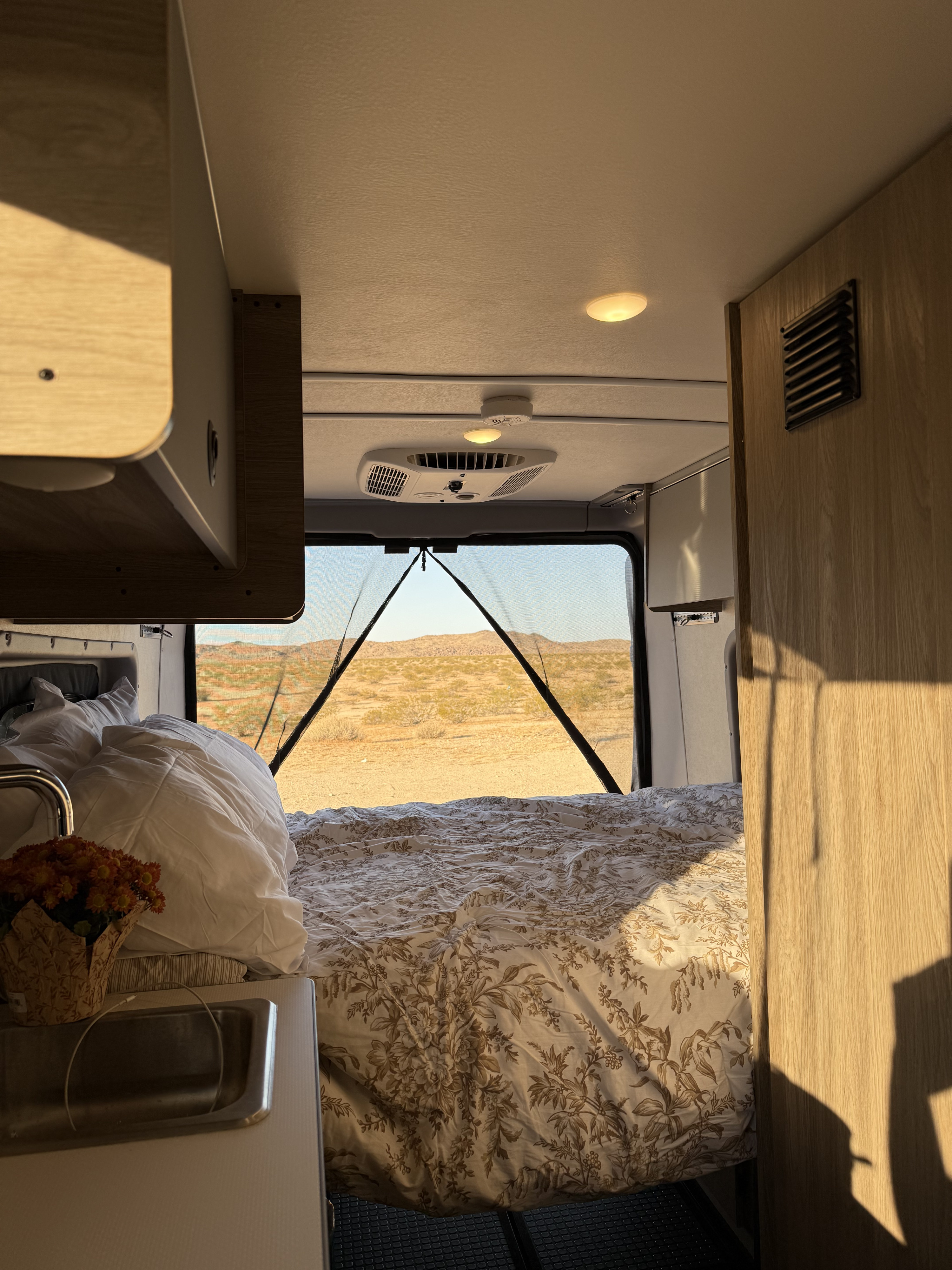 Inviting RV rental interior: a bed with patterned linens, small sink, and mesh screen offering desert mountain views.. Winnebago Solis 59px 2025