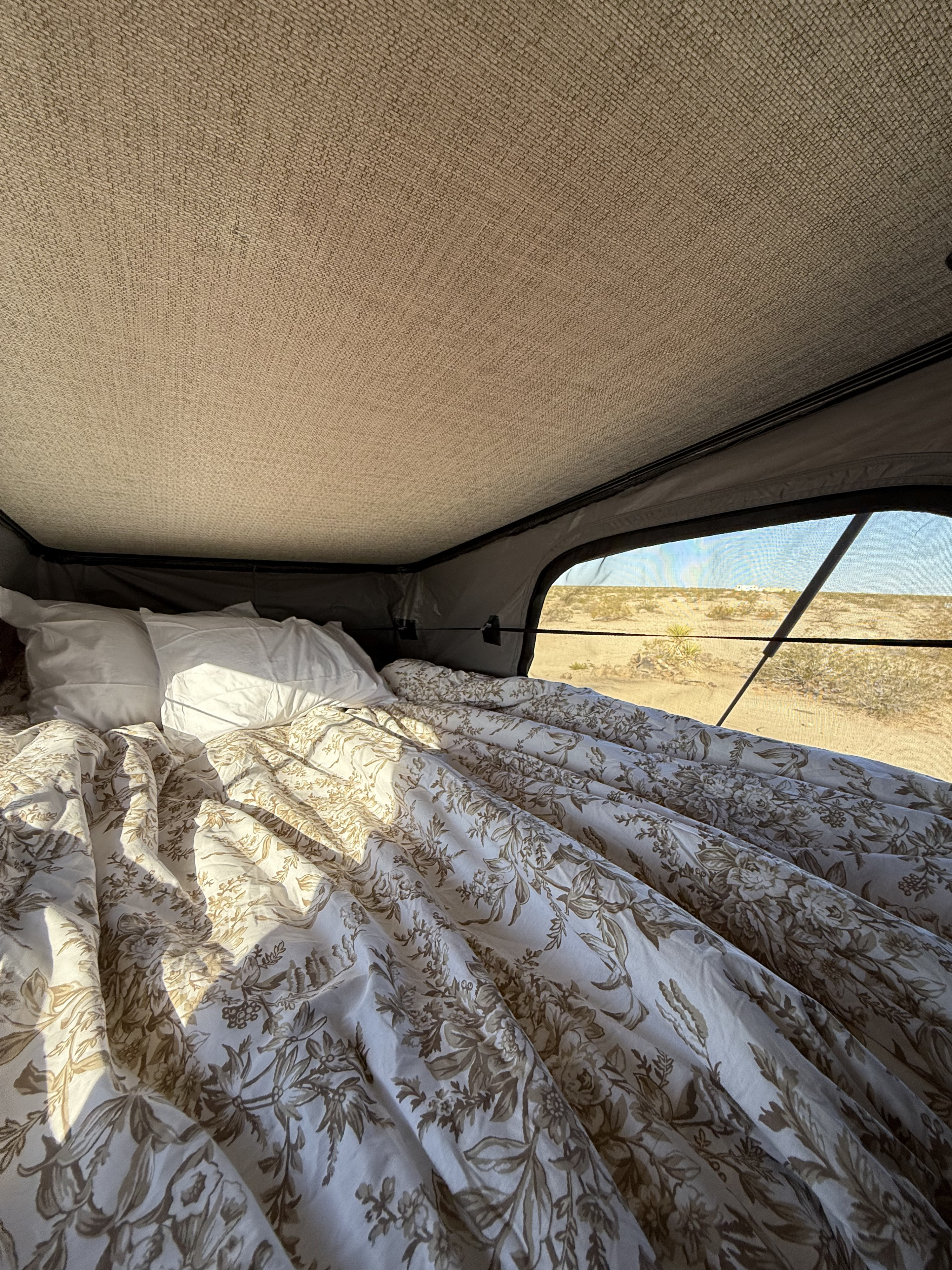 Comfy bed in an rv rental rooftop tent, featuring a floral duvet and panoramic desert views. Ideal for glamping adventures.. Winnebago Solis 59px 2025