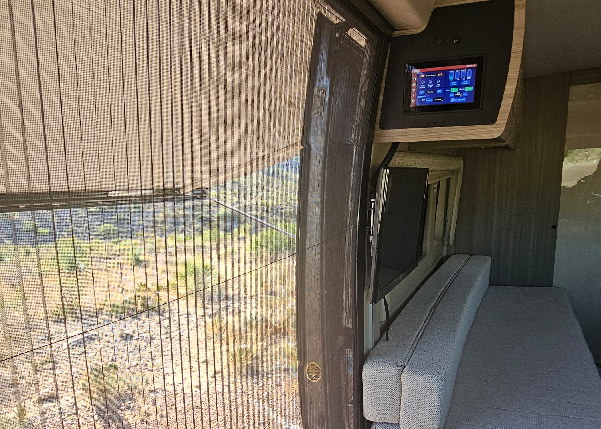 Inside this RV rental: a large window with desert landscape, overhead control panel, TV, and bench seating.. Entegra Coach Ethos 2024