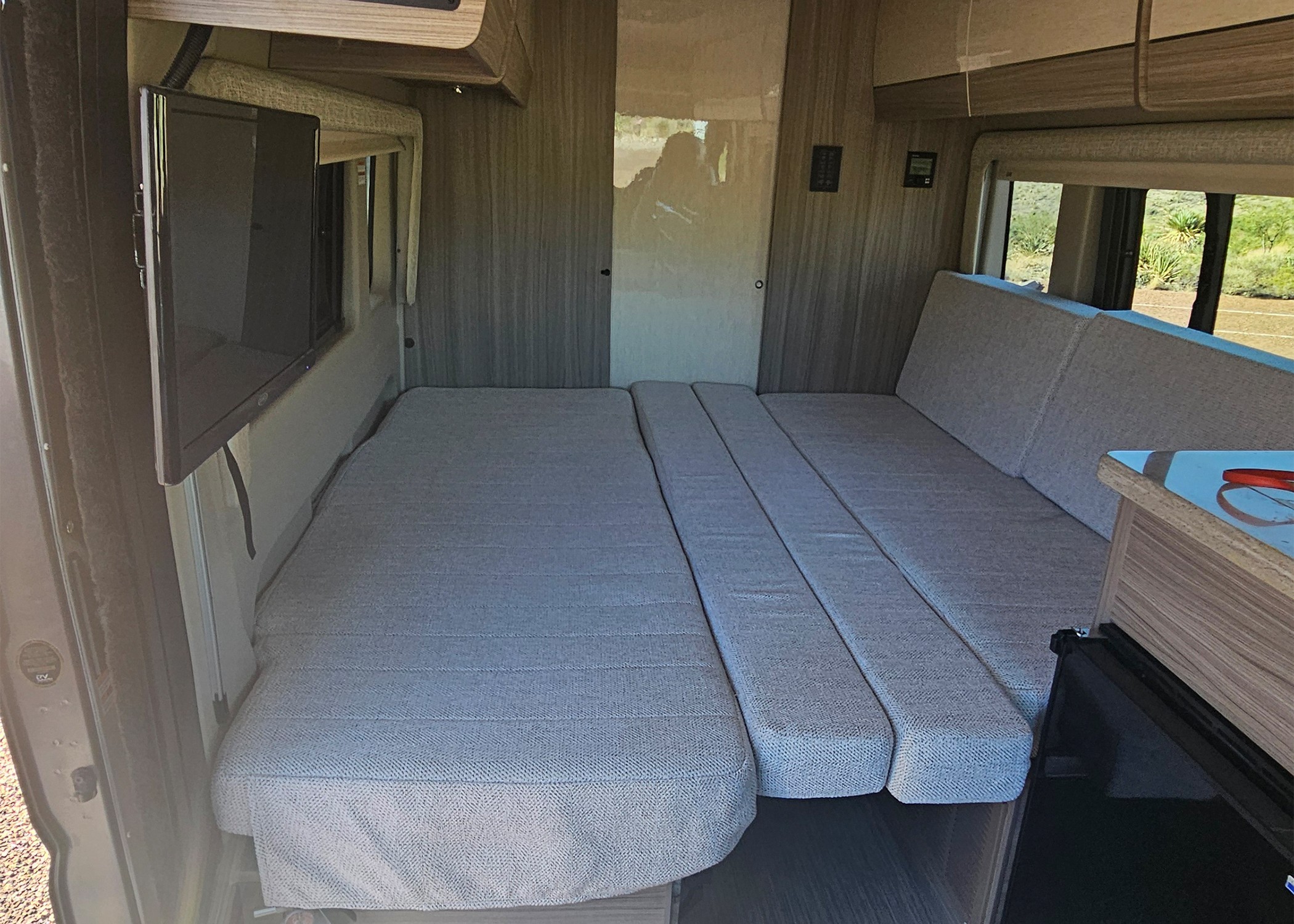 Inside an RV rental: a flexible grey cushion bed/seating area, TV, and scenic rear windows provide comfort on the road.. Entegra Coach Ethos 2024