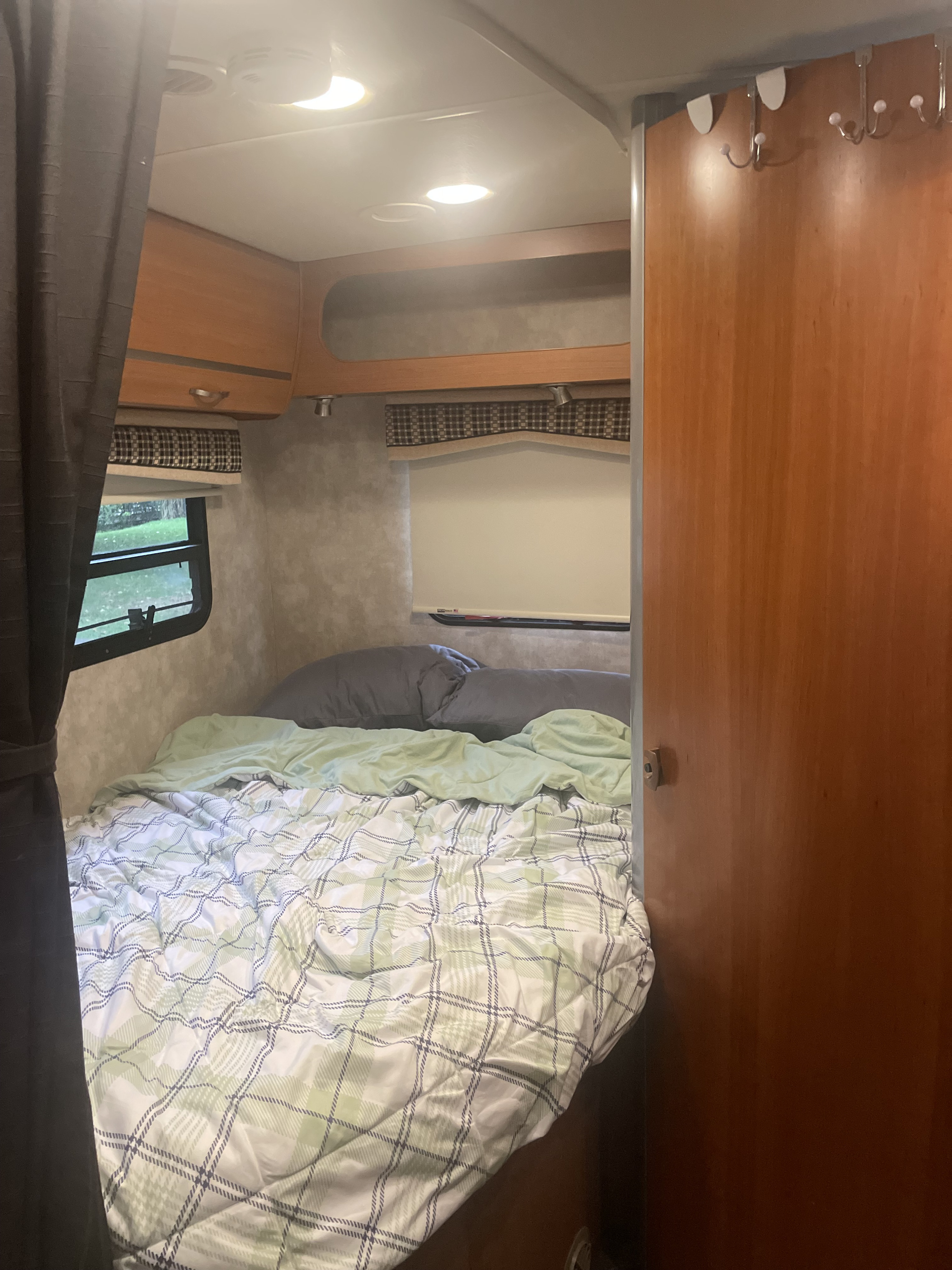 Cozy RV rental bedroom with plaid bedding, overhead cabinets, and a window for comfortable travel lodging.. Itasca Navion 2012