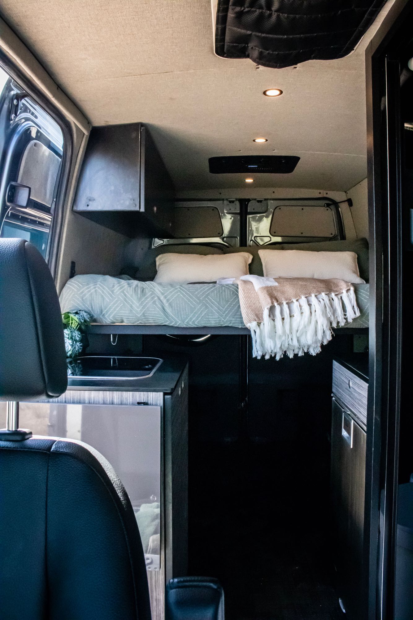 Cozy modern camper van interior for RV rental. Features a comfortable bed, mini-kitchen, and sleek design.. Mercedes-Benz Sprinter 2500 2019