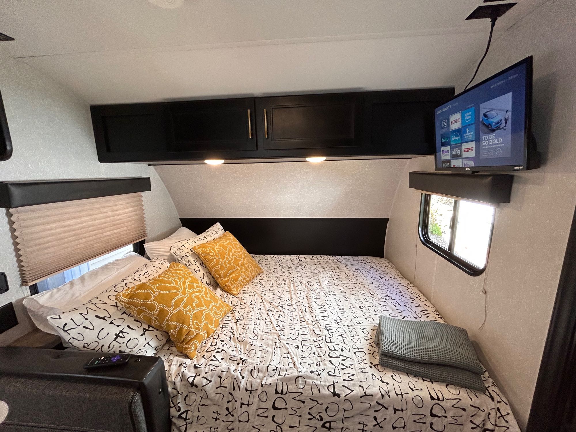 An RV rental's bedroom featuring a unique alphabet-patterned bed, cozy pillows, practical overhead storage, and a mounted TV.. Forest River Cherokee Wolf Pup 2021