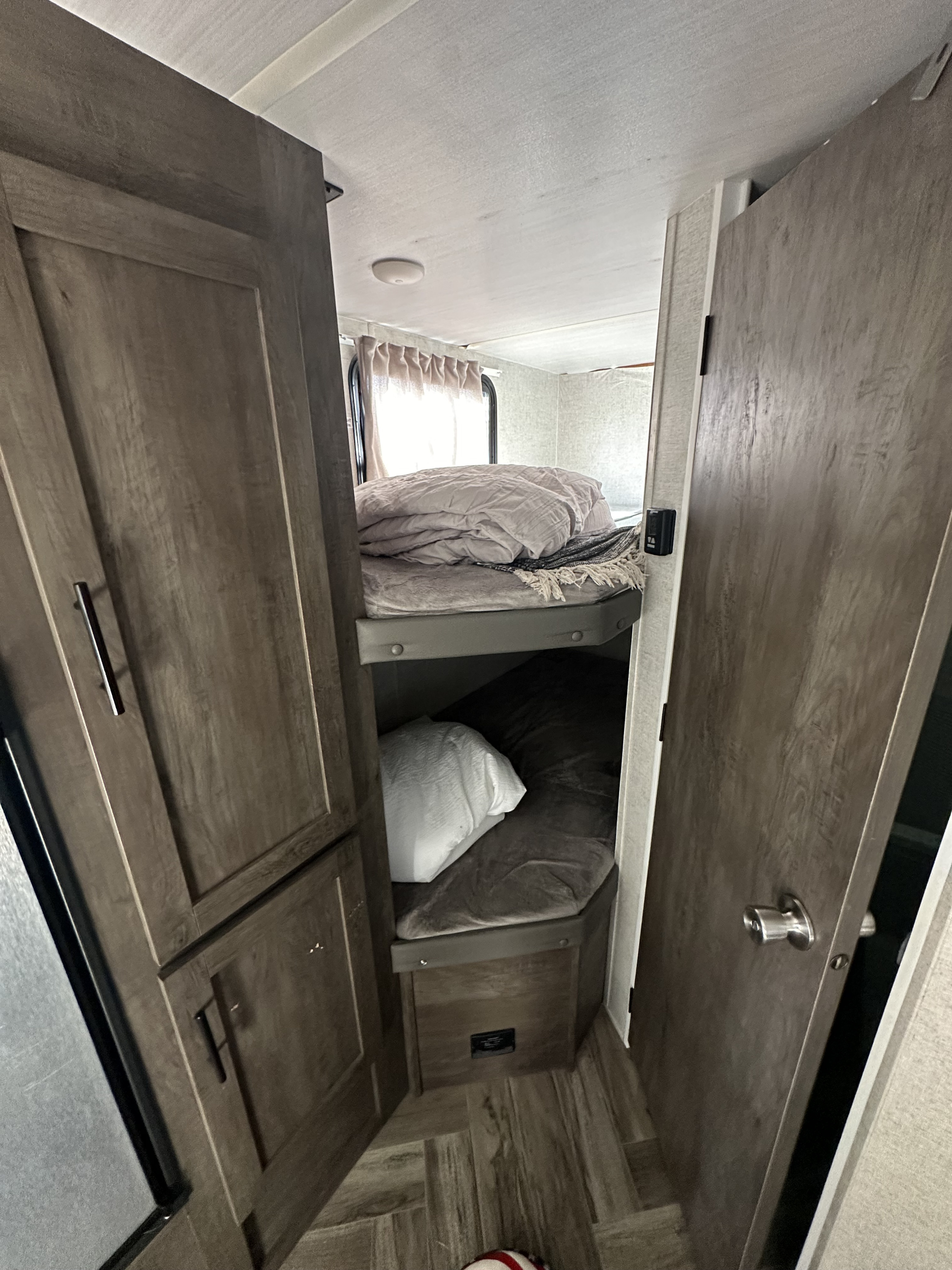 An RV rental interior reveals stacked bunk beds, upper made with a light duvet, lower with a darker blanket. Compact and practical.. Forest River Salem Cruise Lite 2020