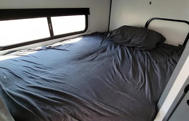 RV rental interior: A dark-sheeted bed with a window offers a cozy space. Note the metal bunk frame.. Keystone RV Bullet Crossfire 2024
