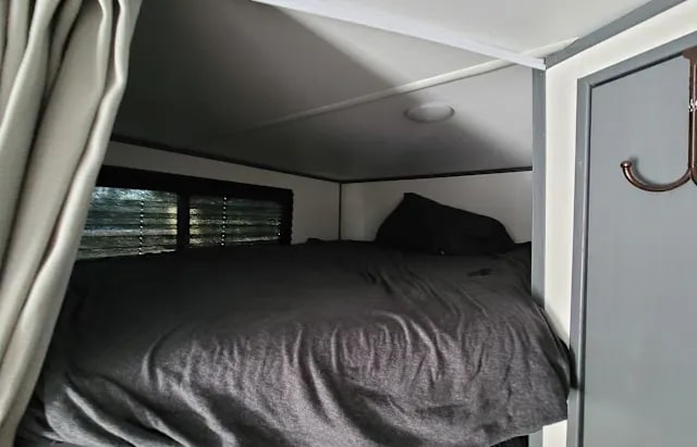 Cozy RV rental sleeping area with a comfortable bed, window with blinds, and convenient coat hooks, perfect for your travels.. Keystone RV Bullet Crossfire 2024