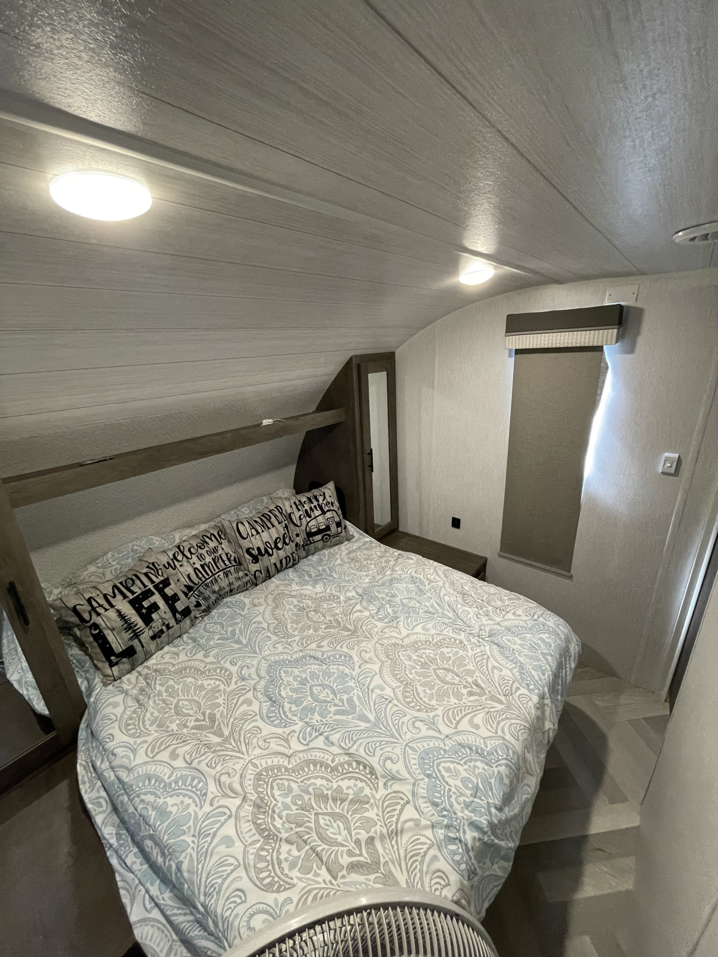 RV rental bedroom featuring a bed with patterned bedding and 'Camping Life' pillows under bright overhead lights.. Forest River Salem Cruise Lite 2022