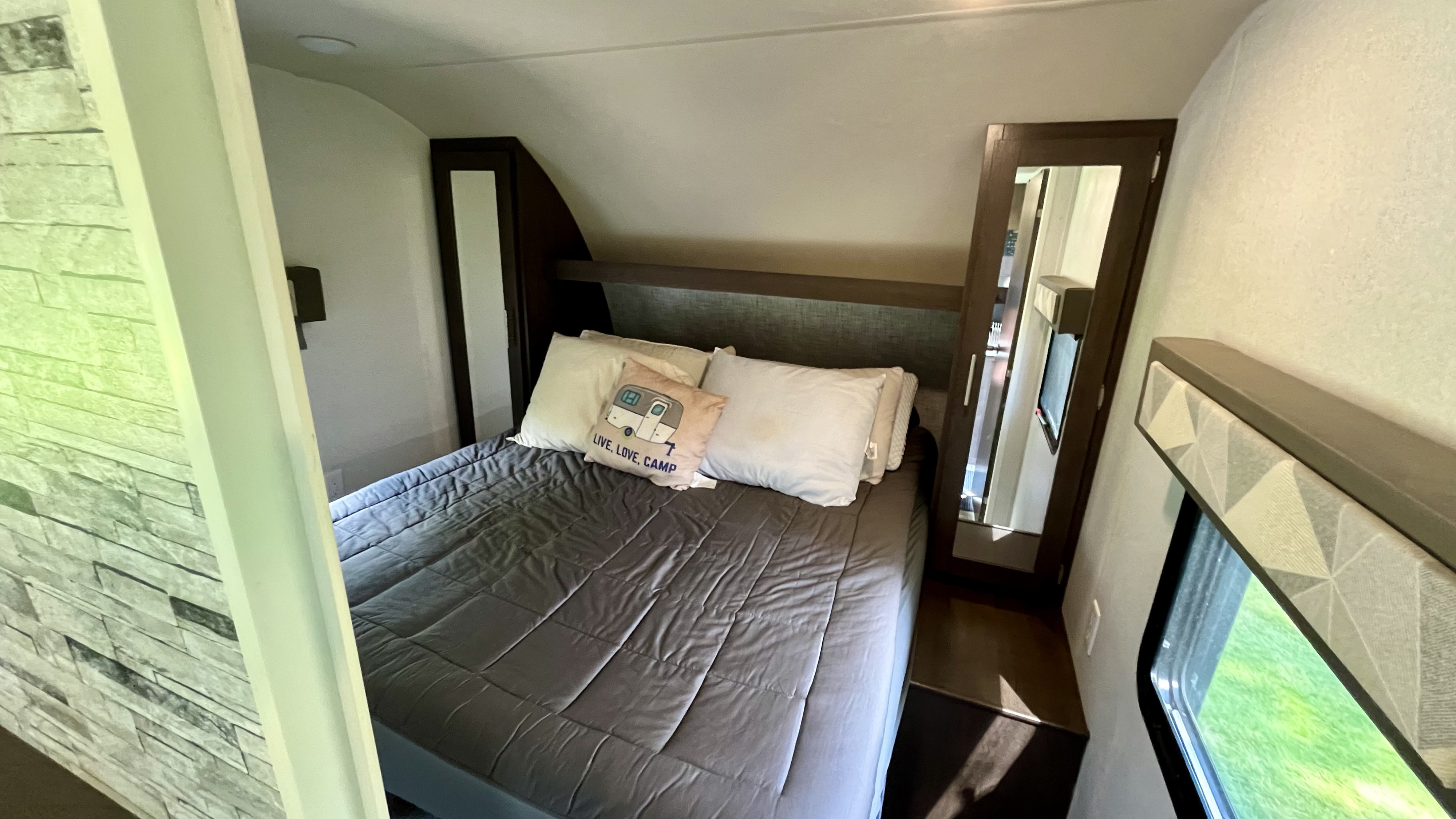Inside a cozy RV rental: a comfortable bedroom featuring a bed, pillows, and built-in storage. Ideal for travel.. Forest River Wildwood 2019