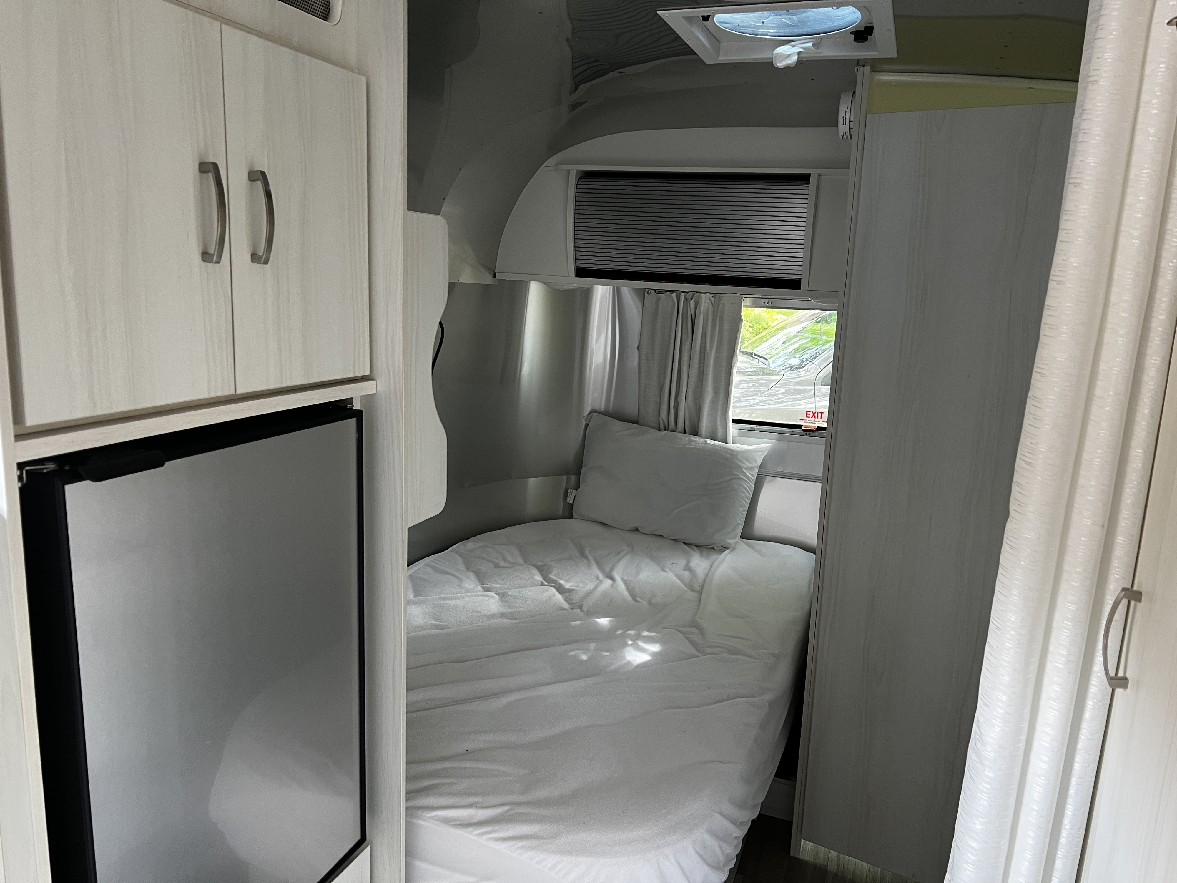 Compact RV rental interior: showing a cozy bed, refrigerator, and ample overhead storage cabinets.. Airstream Bambi 2020