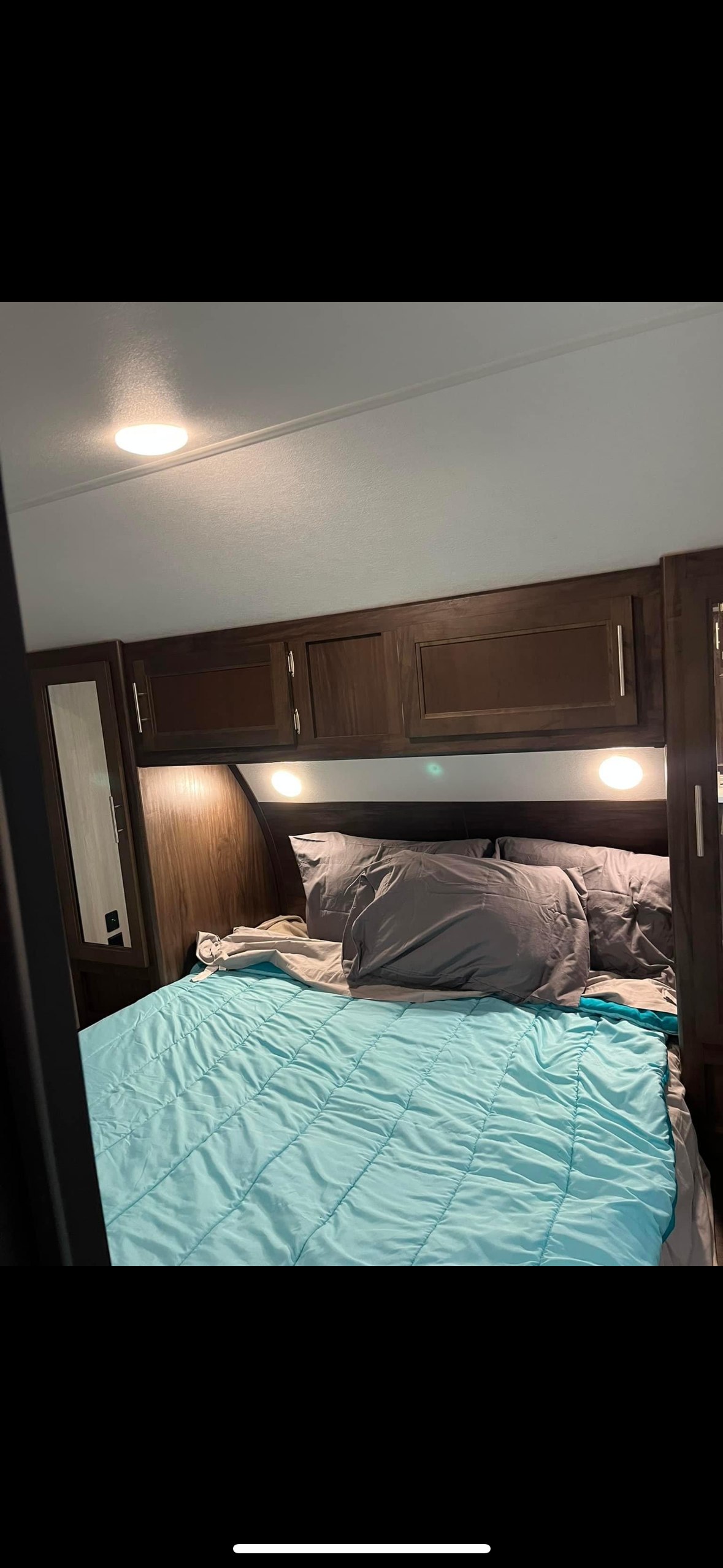 Comfortable RV rental bedroom with a light blue bed, built-in lights, and storage cabinets.. Forest River Cherokee 2019