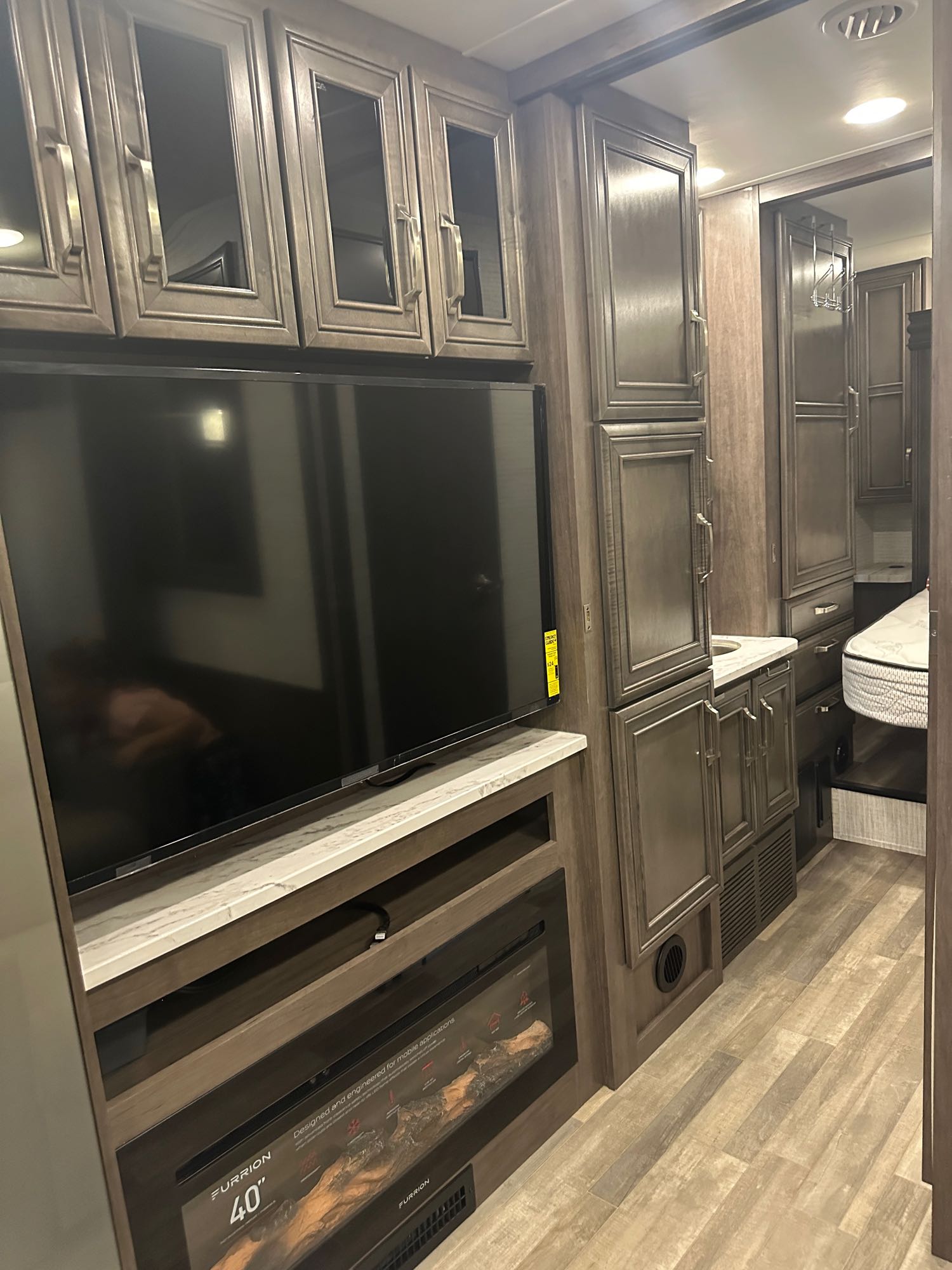 Modern RV rental interior with a living area featuring TV & fireplace, extensive cabinetry, and view into the bedroom.. Jayco Greyhawk 2024