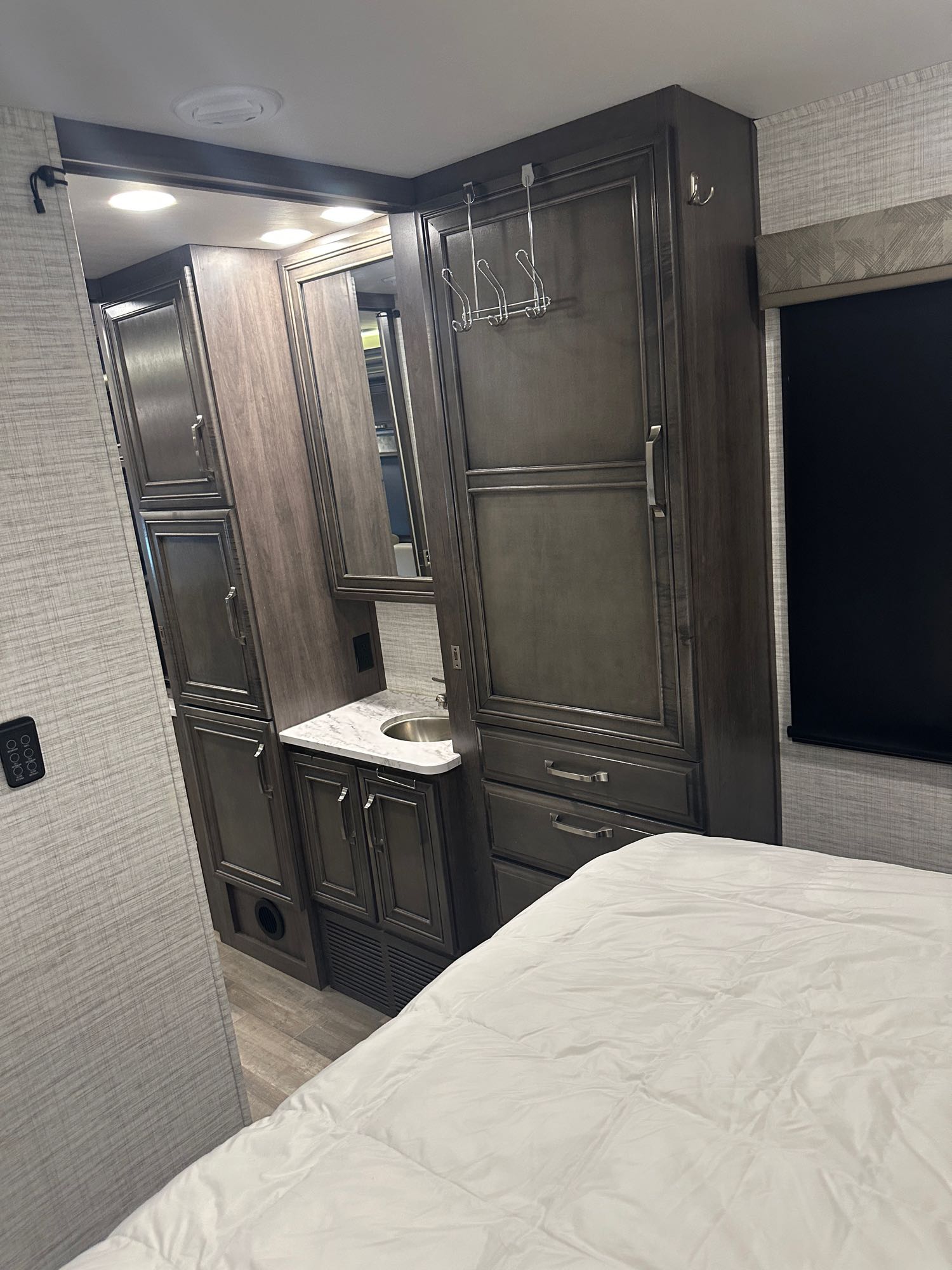 RV rental interior: cozy bedroom with white bedding, dark wood cabinets for storage, and a built-in vanity sink.. Jayco Greyhawk 2024