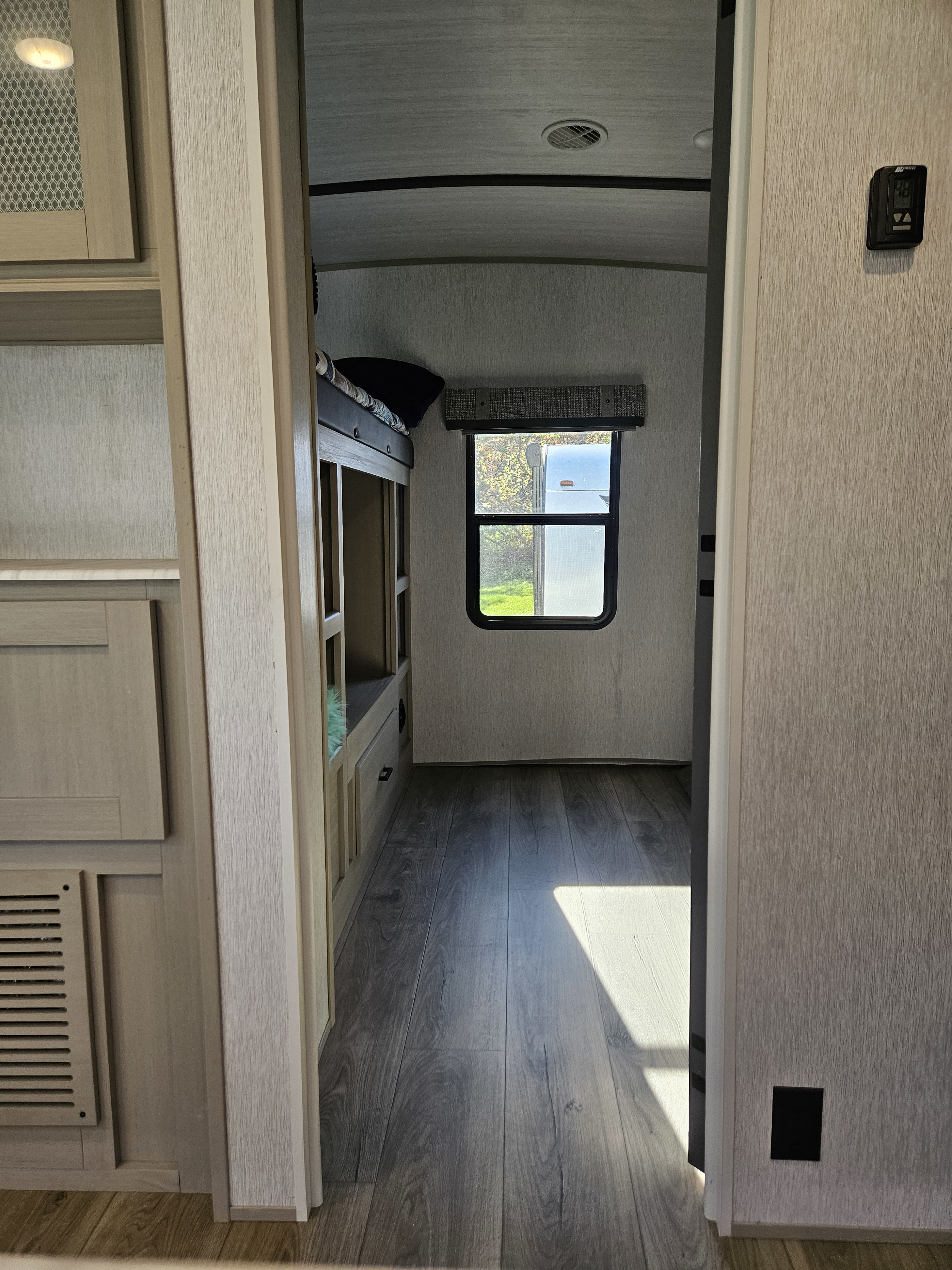 An RV rental's bunk room features stacked bunk beds, a window, and wood-look flooring, viewed from the hallway.. Forest River Heritage Glen 2023