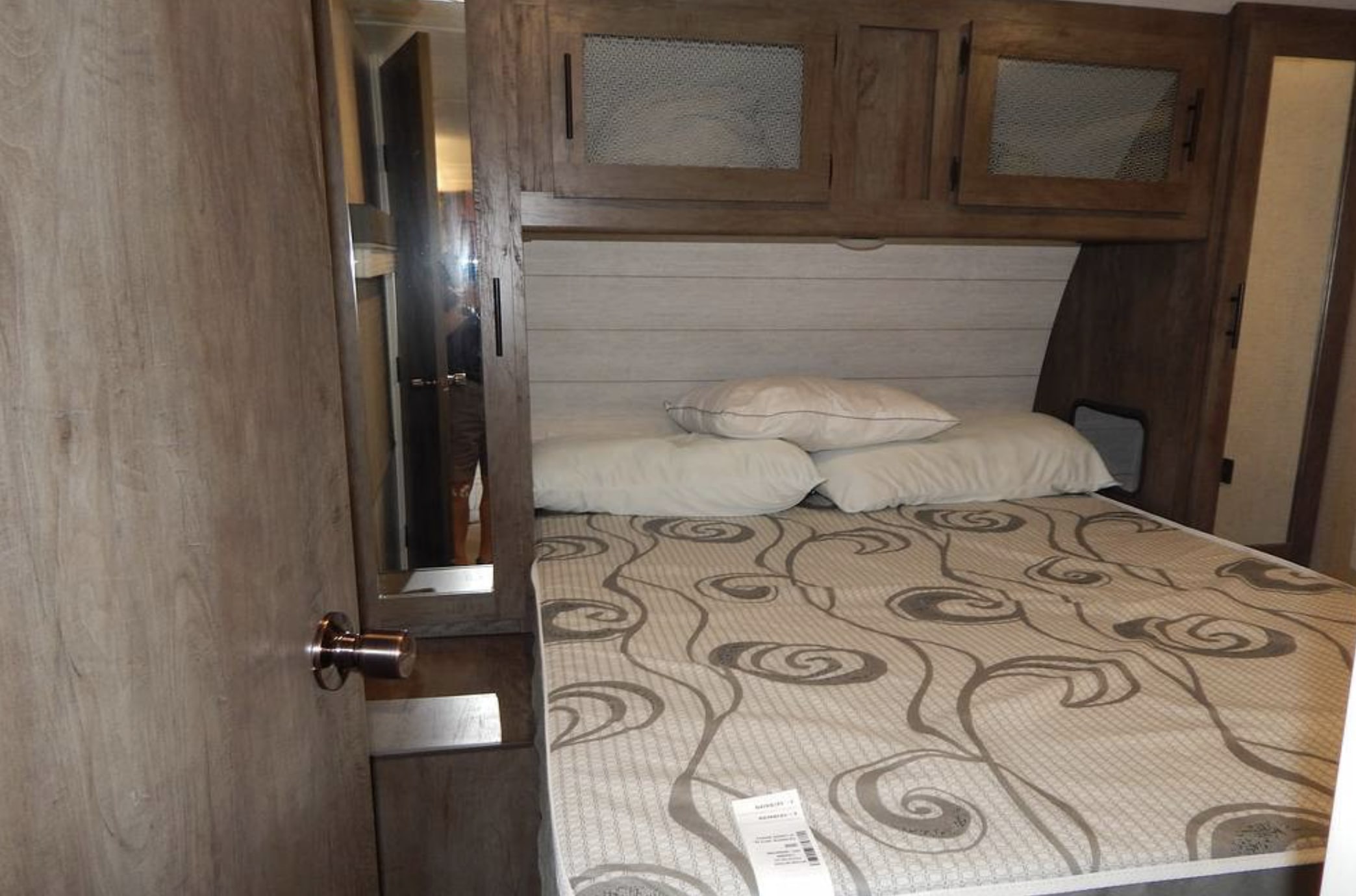 Explore this RV rental's cozy bedroom: a patterned bed, overhead cabinets, and wood-paneled walls.. Forest River Salem 2021