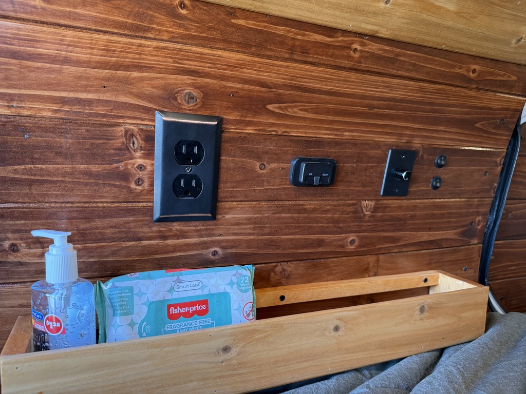 Inside this RV rental, find a rich wood wall with essential power outlets, charging ports, and a handy bedside shelf.. Ford Transit Connect 2020