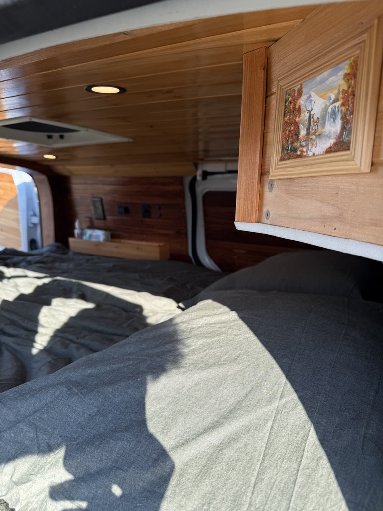 Cozy RV rental interior: wooden ceiling, comfortable bed, and a quaint framed picture.. Ford Transit Connect 2020