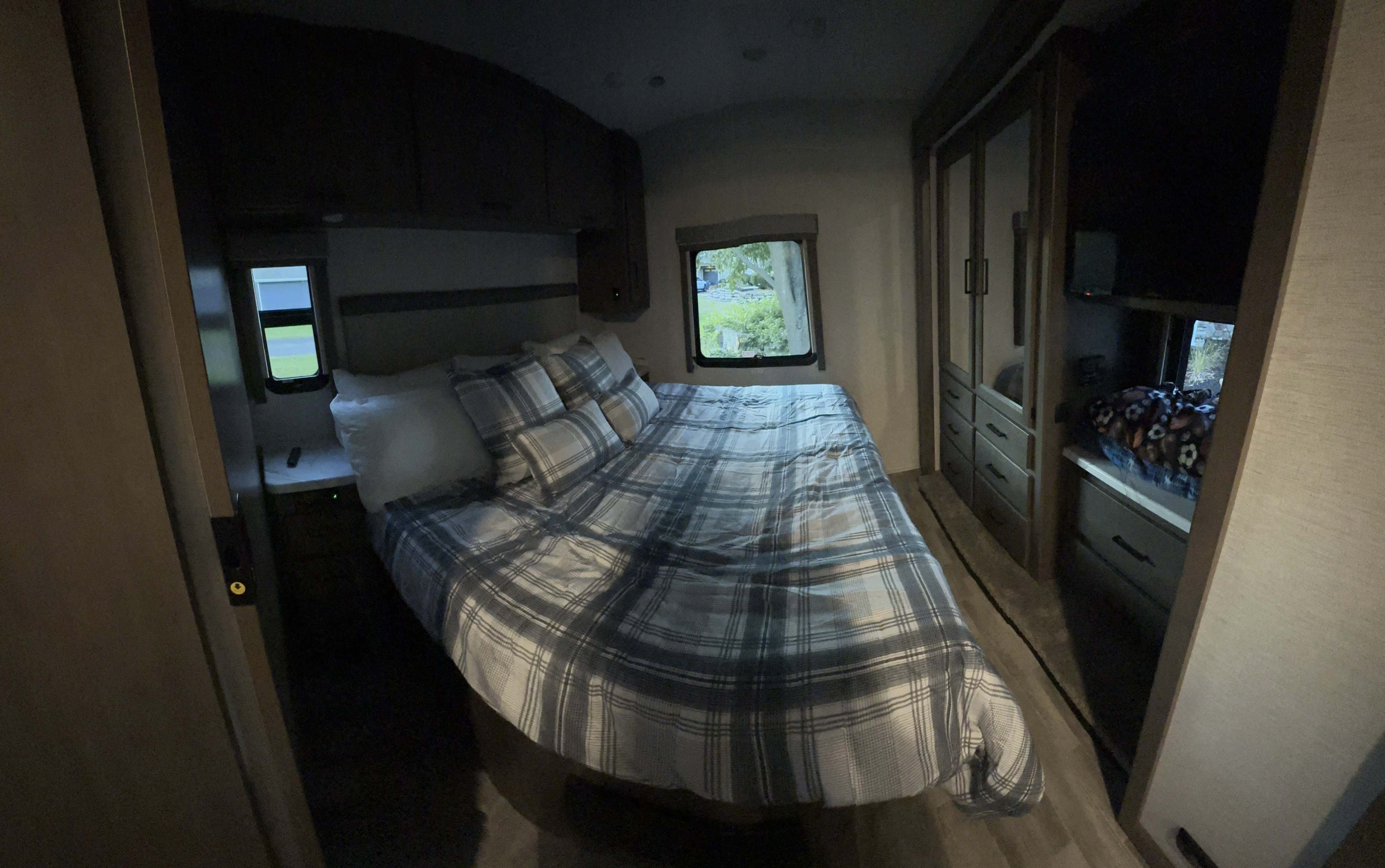 Cozy RV rental bedroom: plaid bed, overhead cabinets, and wardrobe. Windows offer a view. Perfect for your road trip!. Thor Freedom Traveler 2024